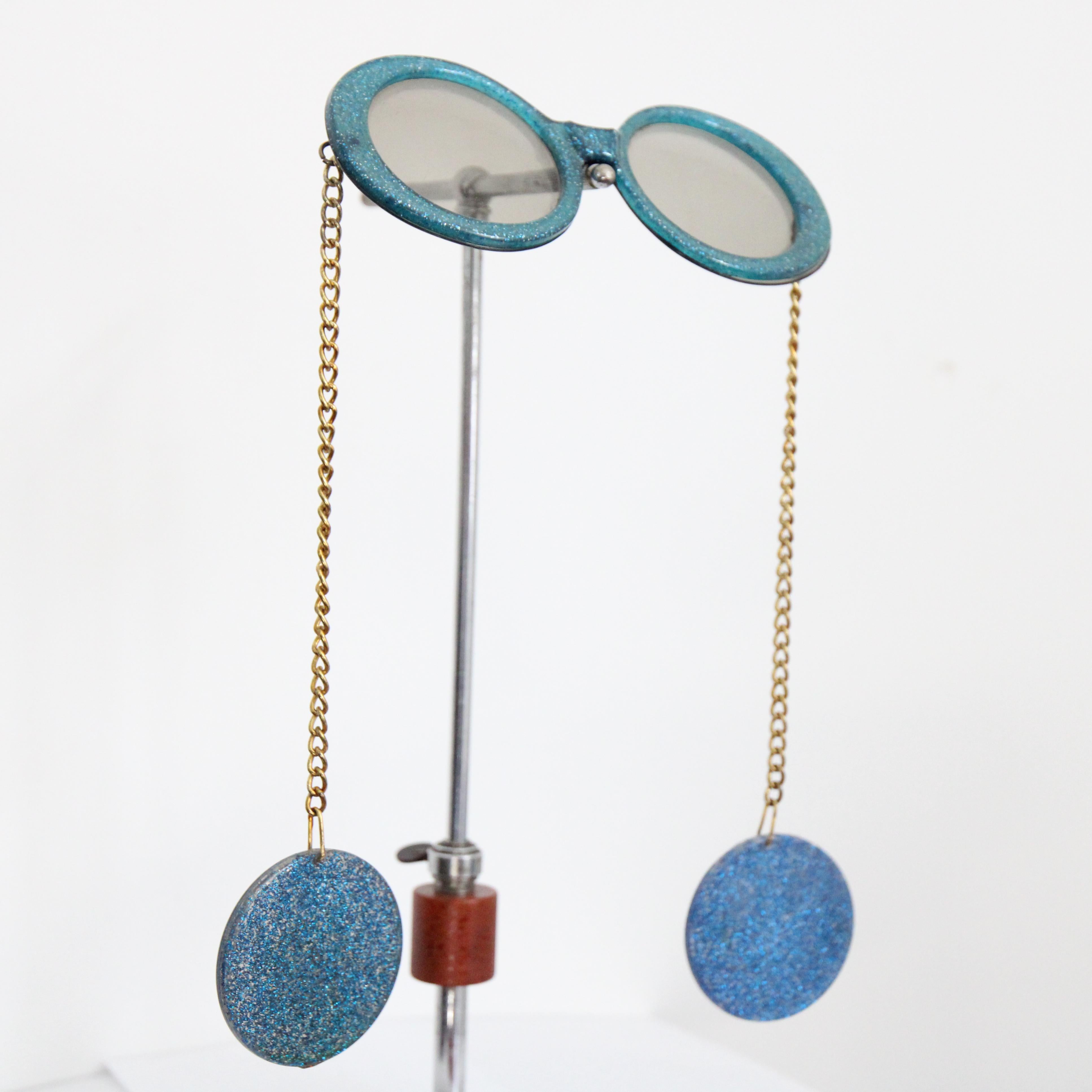 Cette spectaculaire paire de lunettes de soleil des années 1960, d'un magnifique bleu électrique pailleté, est la pièce à ajouter à votre collection d'accessoires. Le pont simple met en valeur le design arrondi de la monture, dont les branches en
