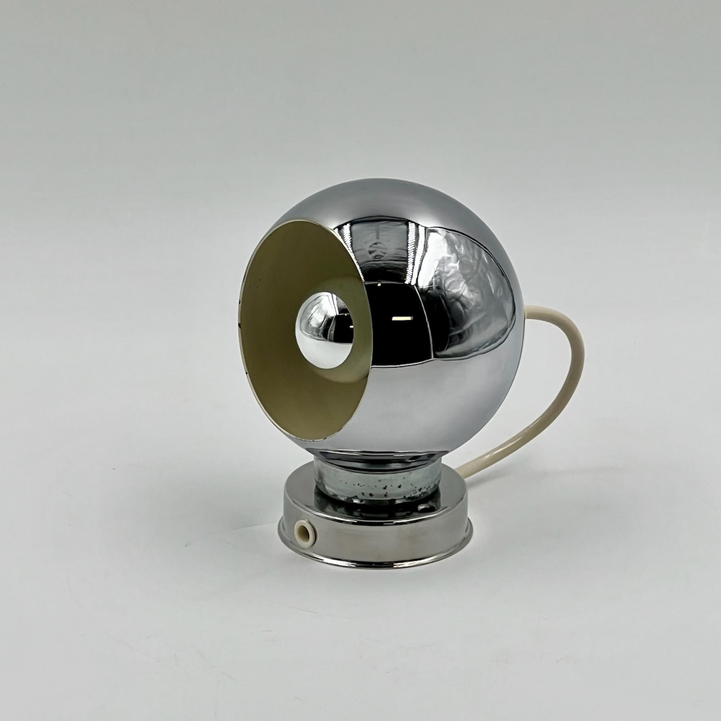 La lampada Reggiani Eyeball incarna l'eleganza del design italiano degli anni '70 e vanta una finitura cromata a specchio che riflette sia la luce che lo stile. Questo pezzo raffinato è dotato di una base magnetica e di una cupola squisitamente