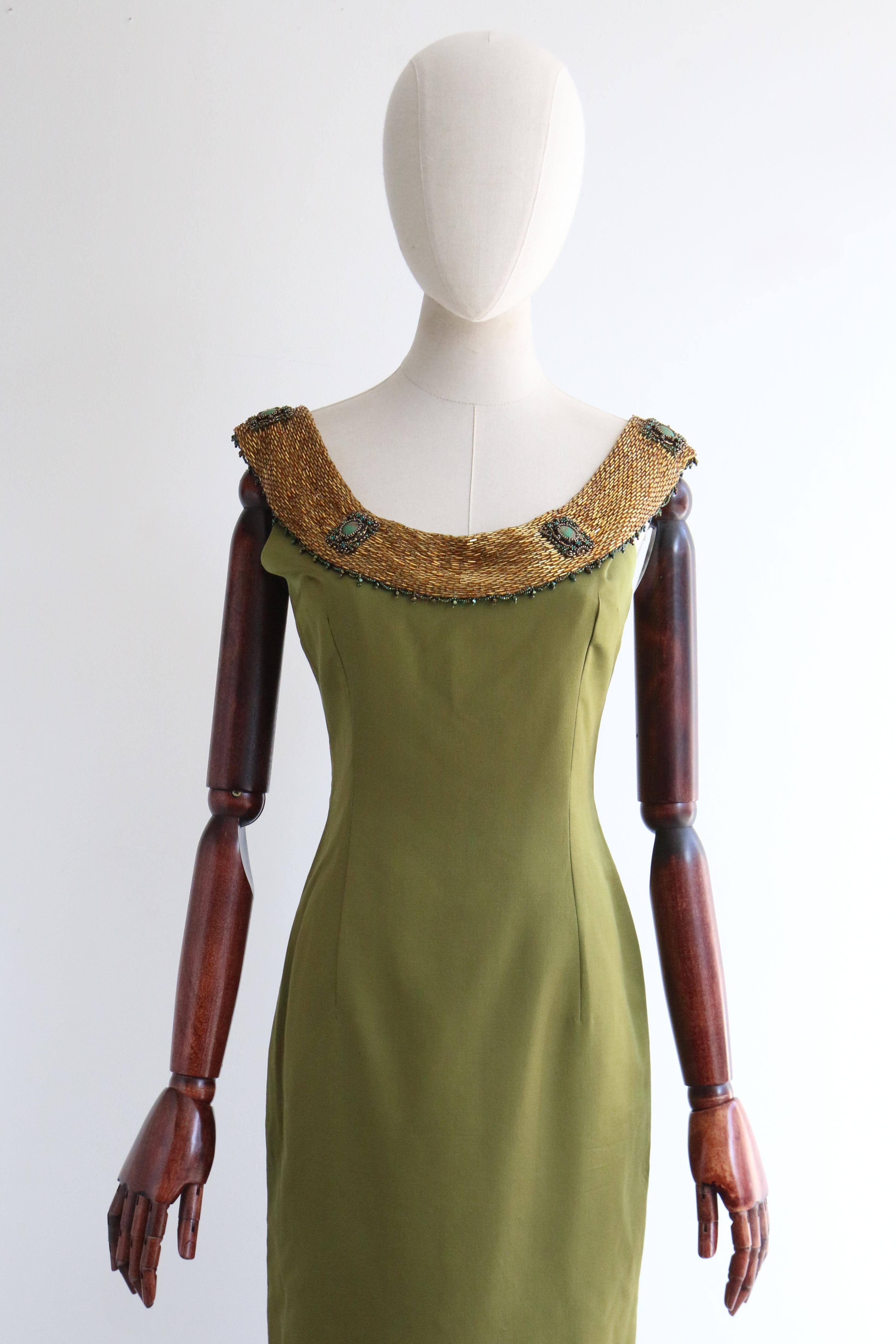 A classic silhouette rendered in a deep shade of olive green silk, embellished with gold and green beadwork, this original 1960's dress is a rare piece to behold and a perfect statement piece for your cocktail wardrobe.

The rounded neckline of the