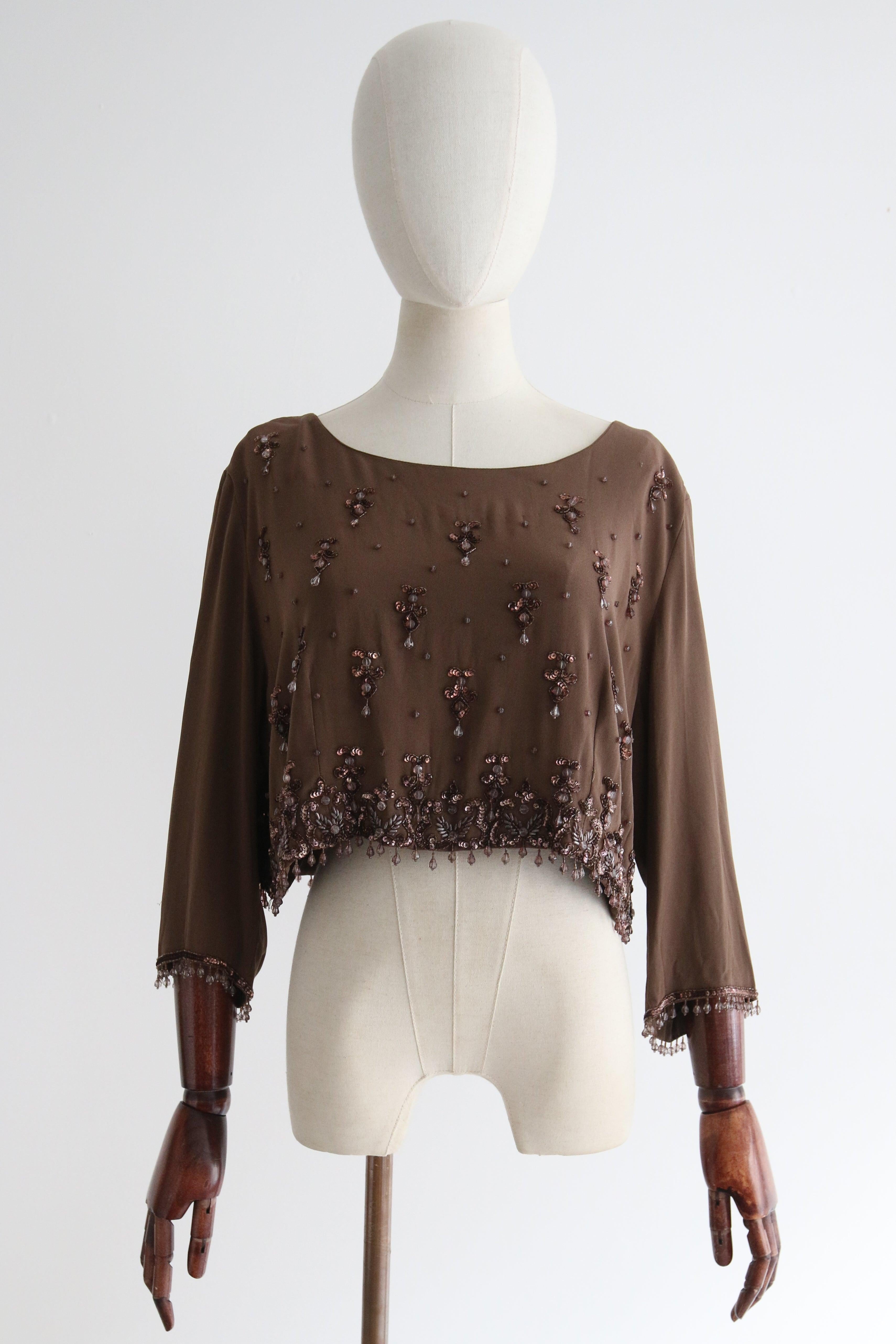 Questa blusa in jersey di seta color acero degli anni '60, impreziosita da paillettes color bronzo, perline di vetro sfaccettate marroni e trasparenti e perline di vetro color bronzo, è stata impreziosita da un'intricata decorazione.  è il pezzo
