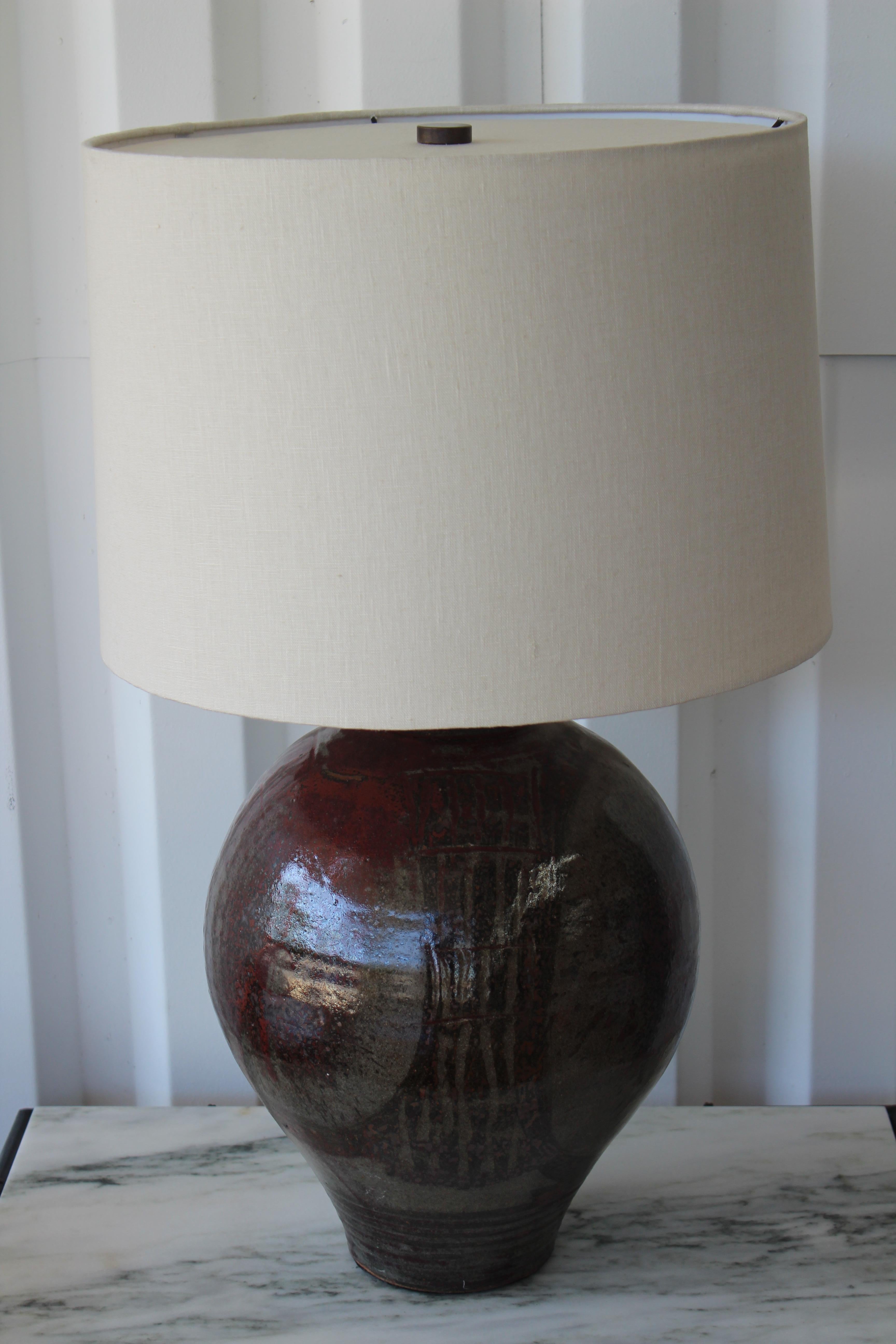 Vintage 1960s studio pottery lamp. Glossy glaze with hues of red. Newly rewired and fitted with a custom linen shade. 
28 H with shade, 13 inches at widest point of the base. Lamp shade is 16