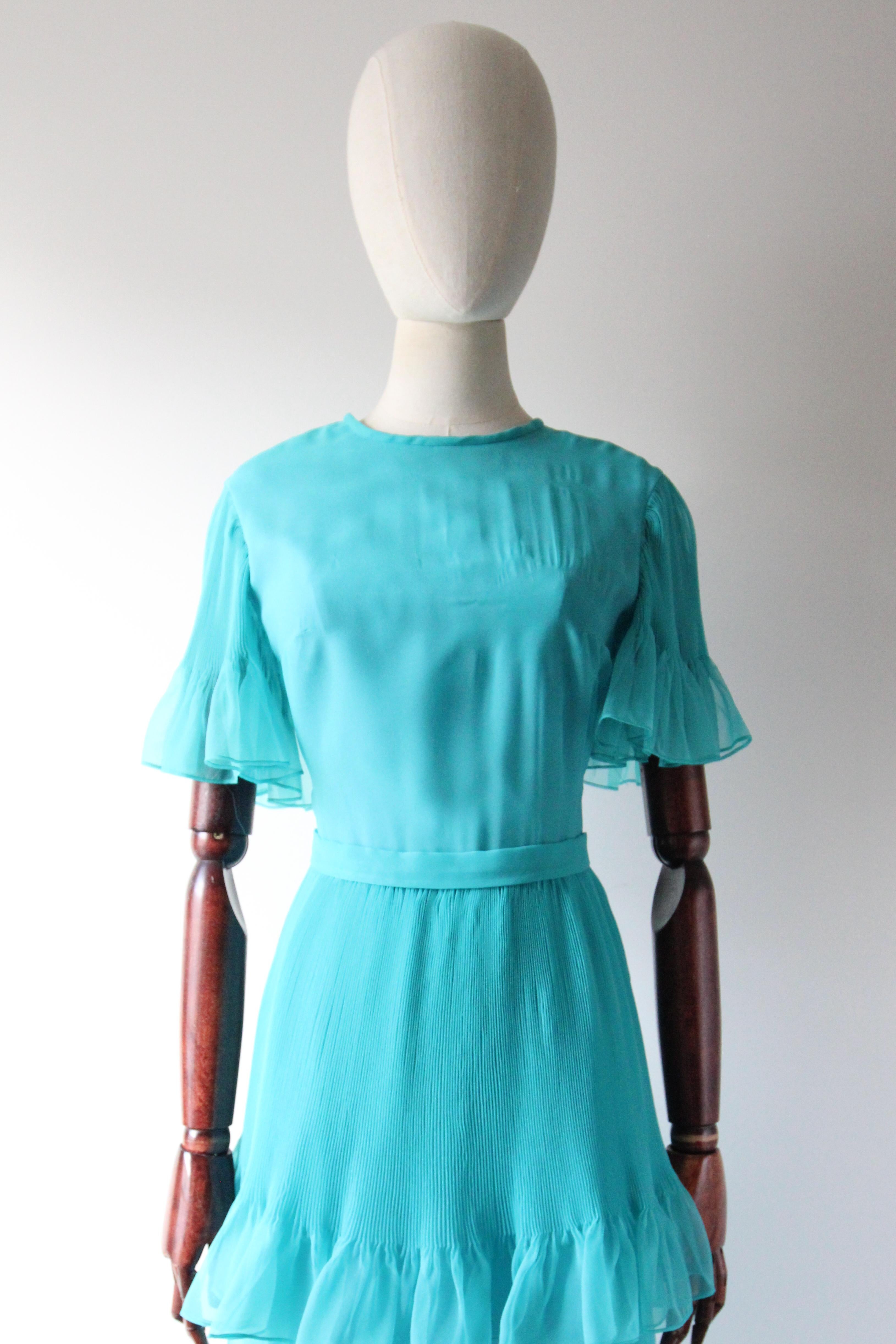Dieses originelle Faltenkleid aus den 1960er Jahren in einem leuchtenden Türkisblau ist ein echter Hingucker und genau das richtige Stück für Ihre Vintage-Sammlung. 

Der elegante Rundhalsausschnitt wird von einer schlichten Schulterlinie
