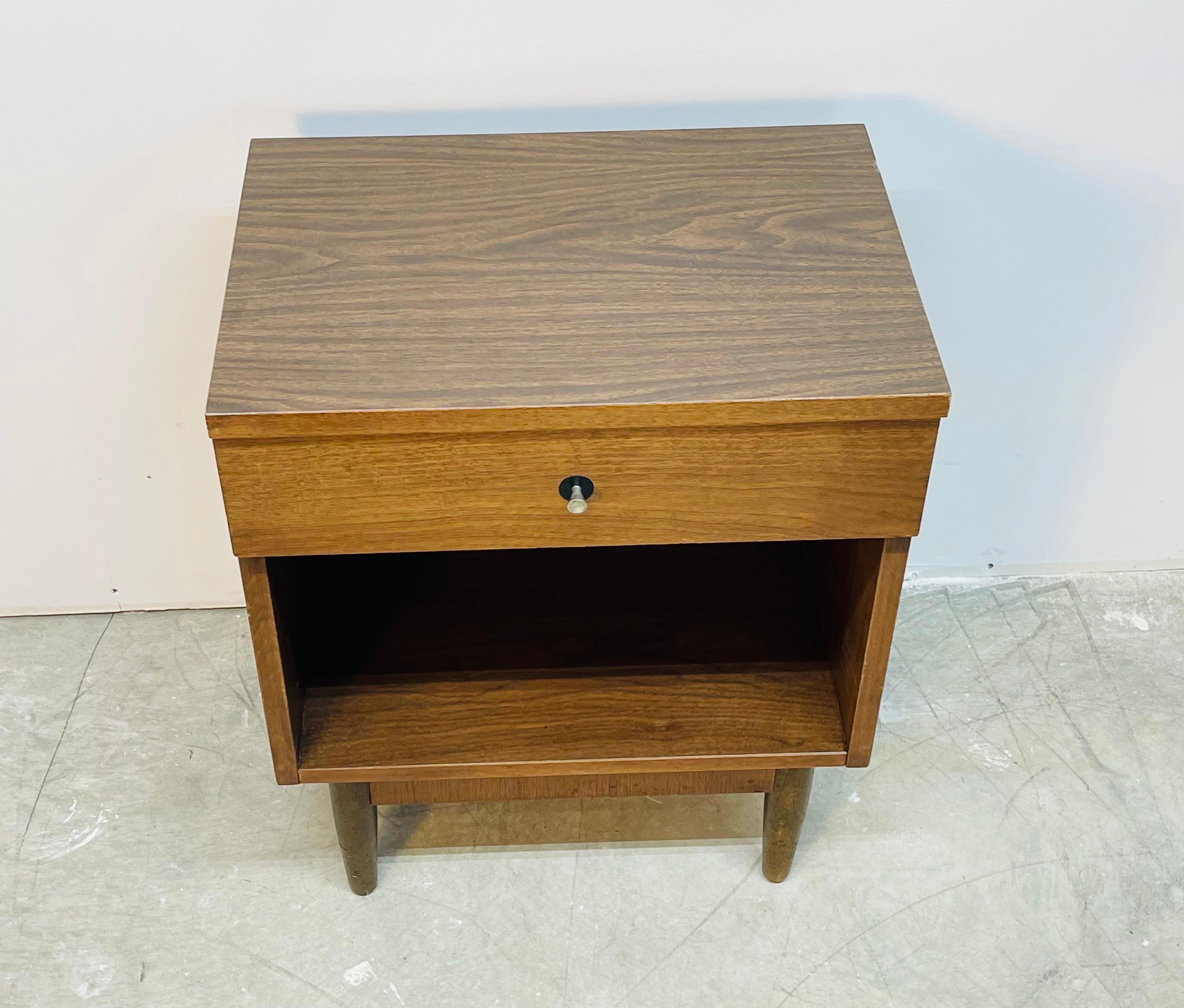 Vintage 1960s walnut wood and laminate top nightstand. The nightstand has a single drawer for storage. There is also open space for additional storage. No marks.