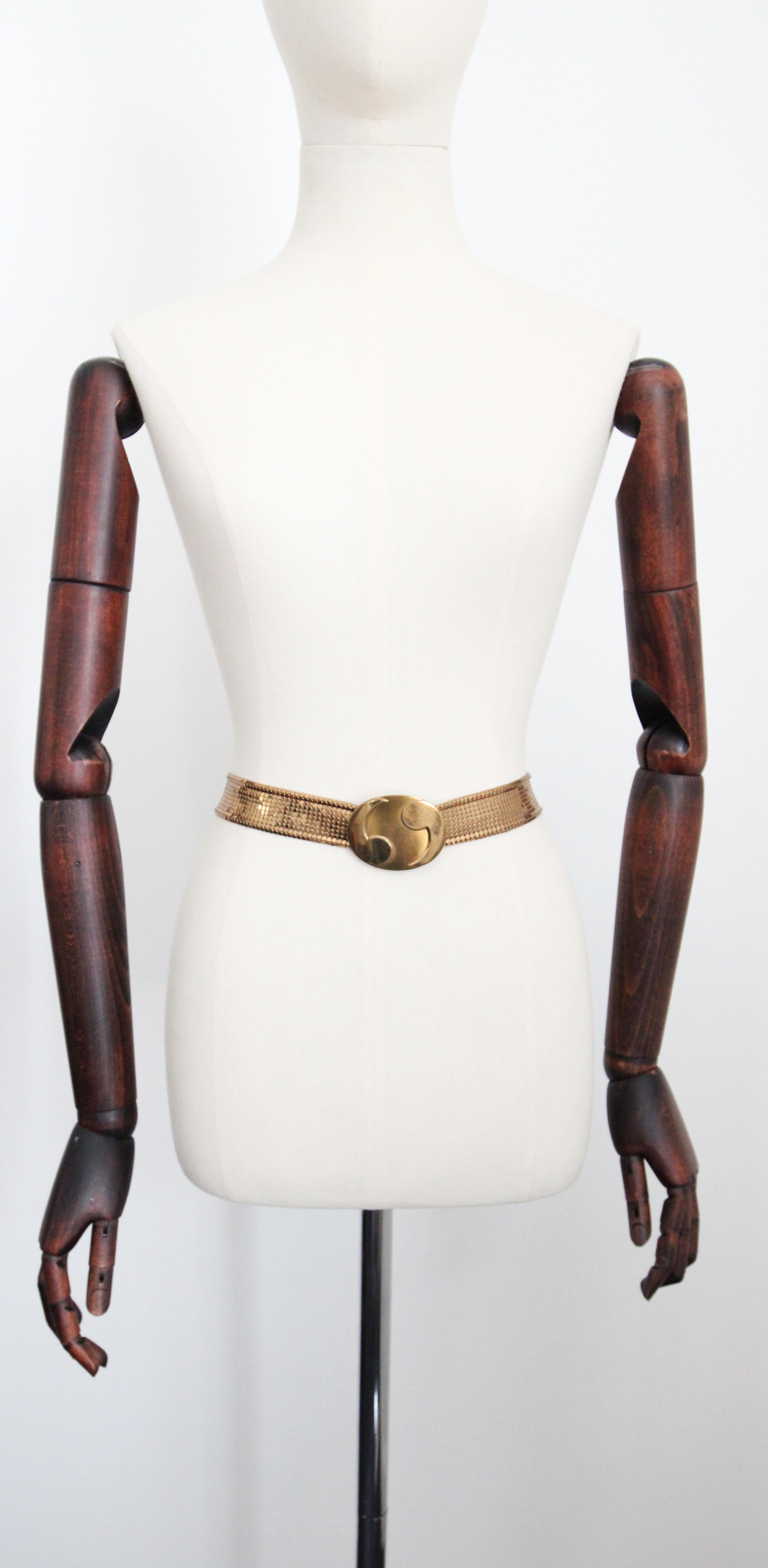 Dieser ikonische Gürtel von Whiting & Davis aus den 1960er Jahren mit einer zentralen Yin- und Yang-Schnalle, die auf beiden Seiten von einem goldenen Netzgürtel eingerahmt wird, ist das perfekte Einzelstück für Ihre Sammlung. 

Messung des