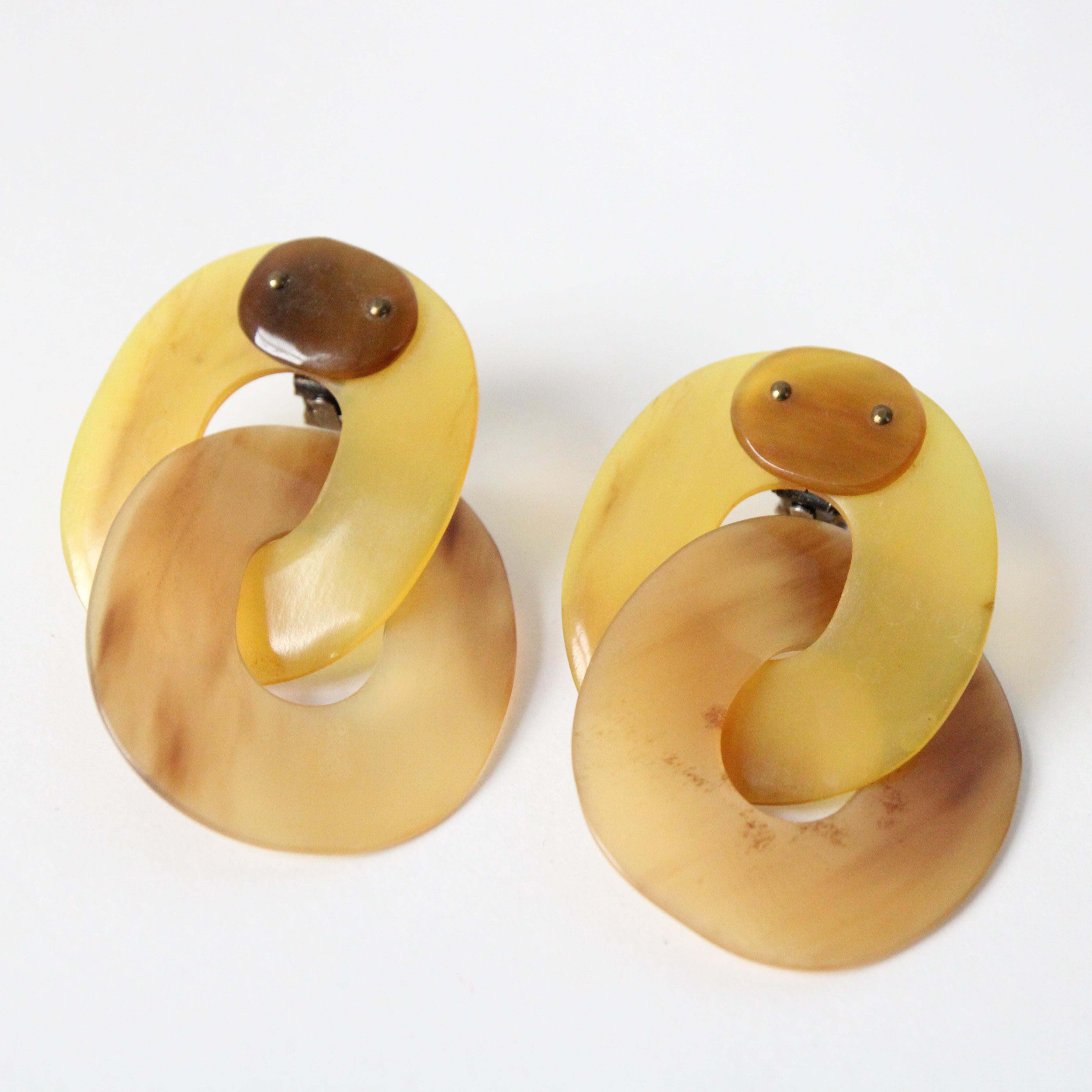 This wonderful pair of 1960's clip on earrings, rendered in a palette of yellow and amber are the perfect set to complete your outfit. The large statement lucite hoops link together and join the clip on fastenings beneath a fixed horizontal oval.