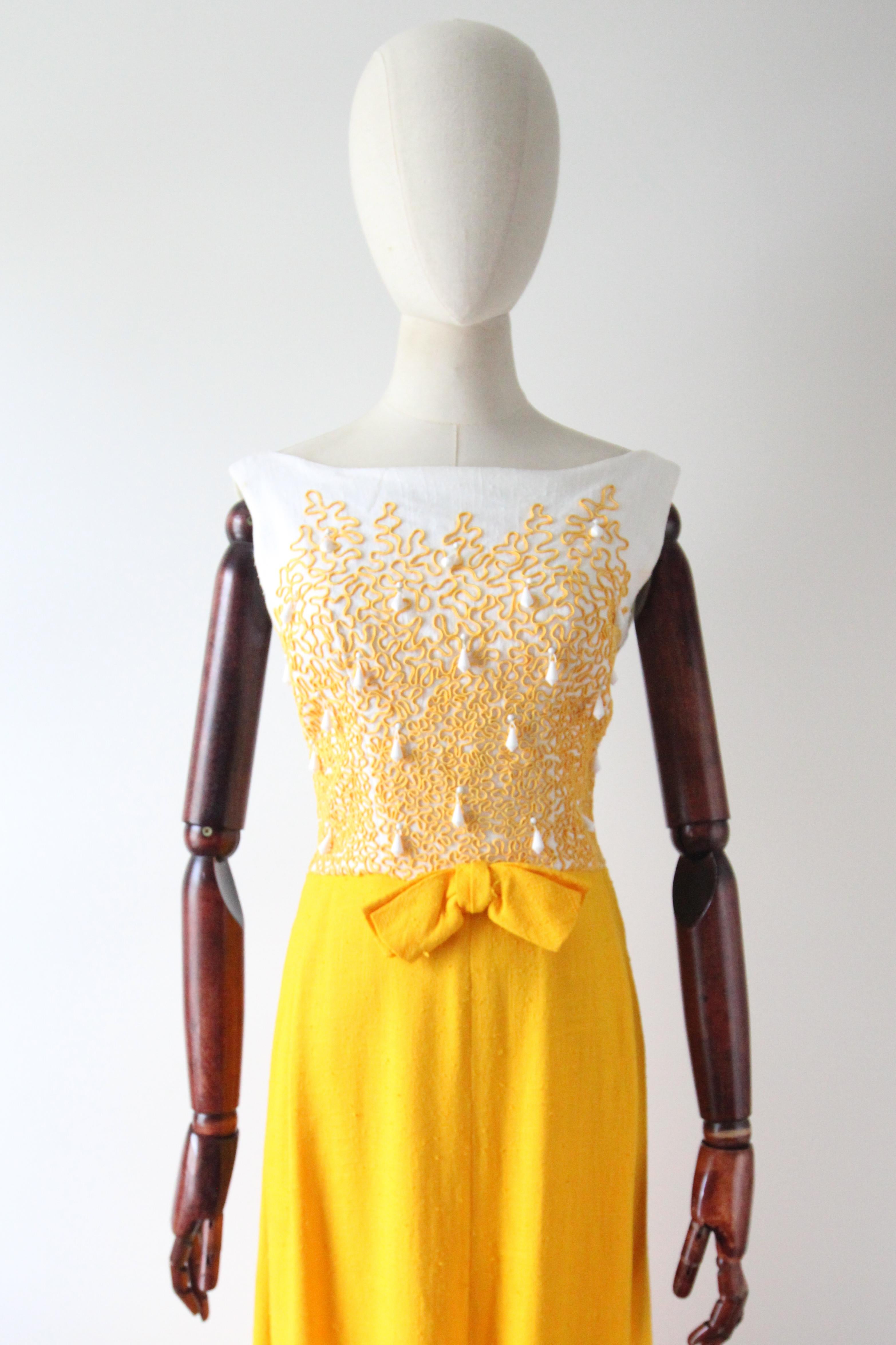 This truly eye-catching 1960's dress, rendered in the most vibrant shade of amber yellow woven cotton, set against a white woven cotton bodice, which is in turn embellished with trailing soutache tape work, and milk glass faceted droplet beads, is