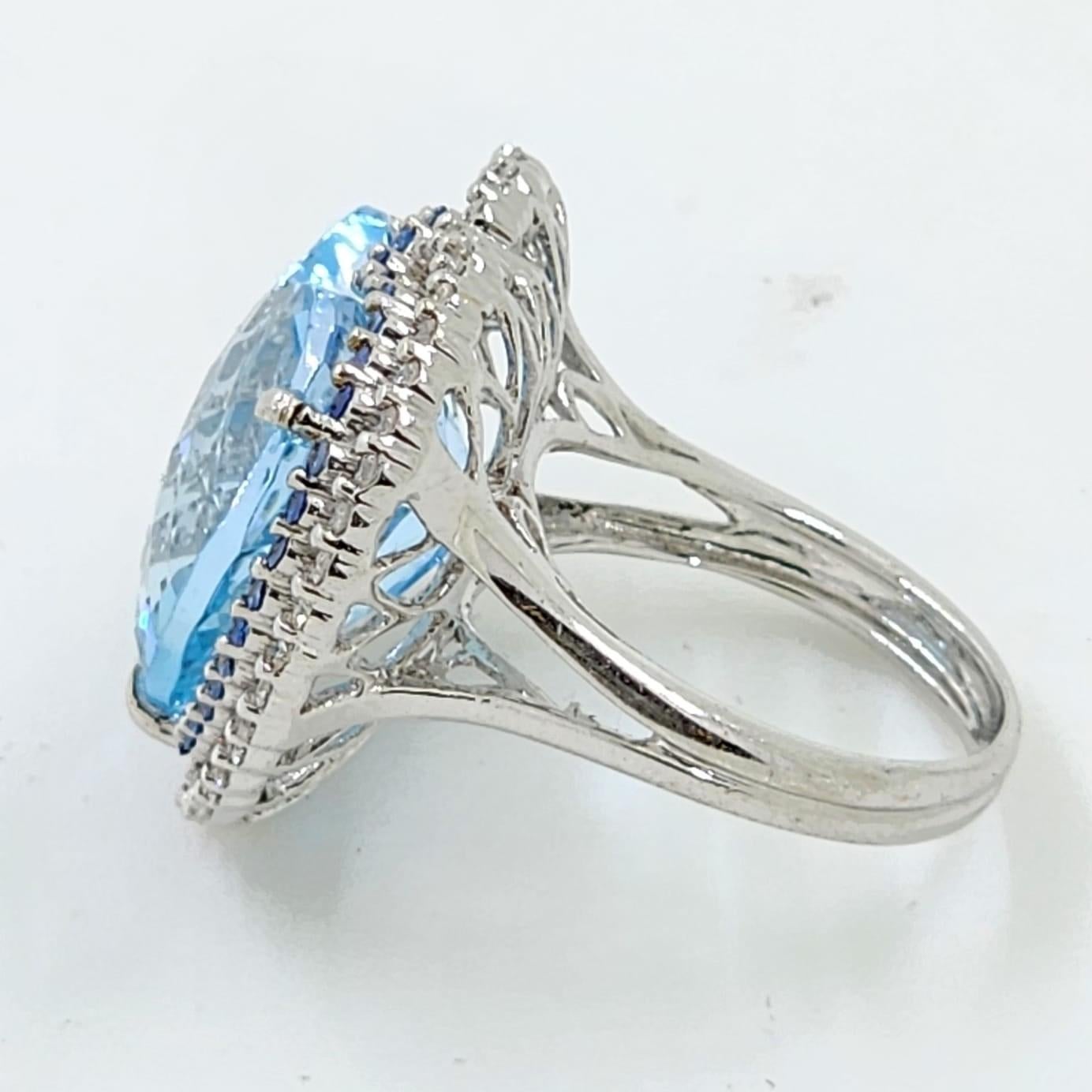 Dieser Ring enthält einen 19,68 Karat Blautopas, der in 2 Diamant-Halos eingefasst ist. Der erste Halo ist mit einem blauen Saphir von insgesamt 0,37 Karat besetzt. Der zweite Halo ist mit weißen runden Diamanten von insgesamt 0,39 Karat besetzt.