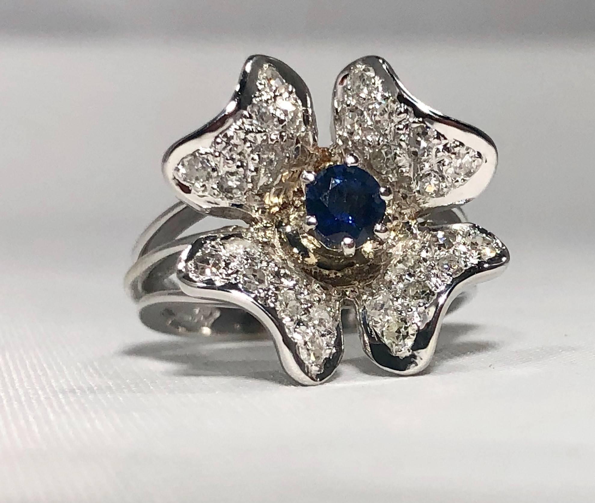 Vintage 1970's 14 karat Sapphire and diamond flower cocktail ring. This is a vintage creation approx. Circa 1970. This piece is created in 14 karat white gold and weighs 6.5 grams, 4.2 dwt.. A full cut round 0.36 carat  Sapphire is the center stone