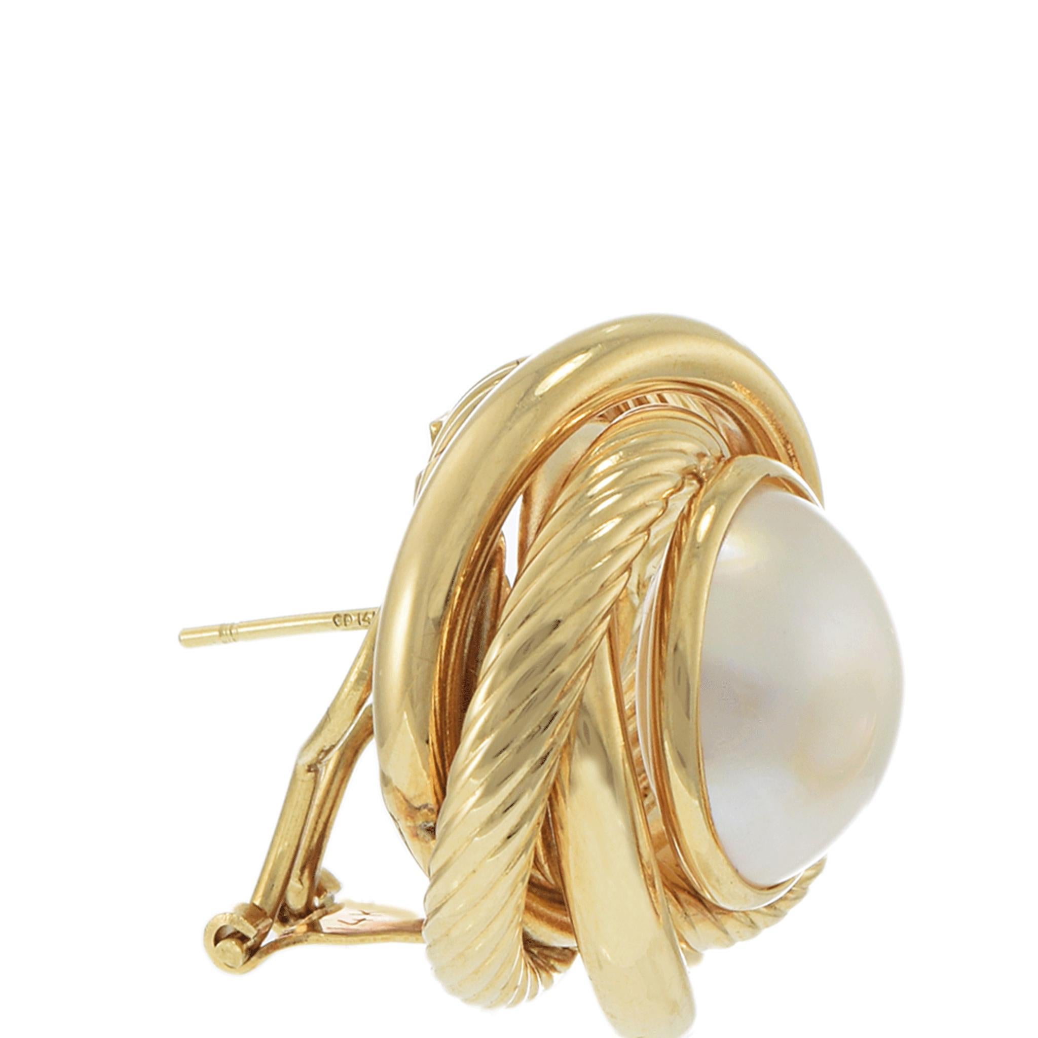 These vintage 1970s earrings frame lustrous 15mm mobe pearls in a sophisticated swirl of polished and textured 14KT yellow gold. The layered design blends smooth curves with rope detailing for a refined sense of movement and depth. Understated yet