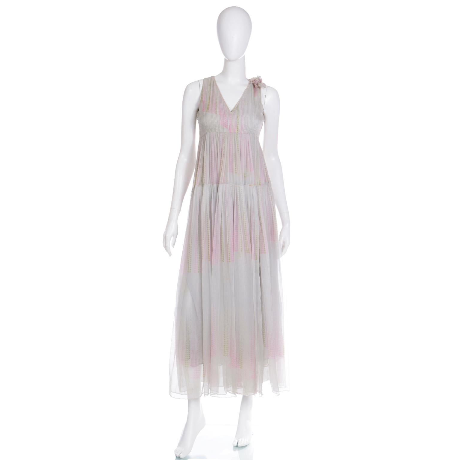This incredible vintage early 1970's André Laug silk chiffon dress is in a pleated multi layered, tiered sheer pale grey silk chiffon with abstract pink and green dots. The bodice has an empire bust and there is a silk flower attached to one of the