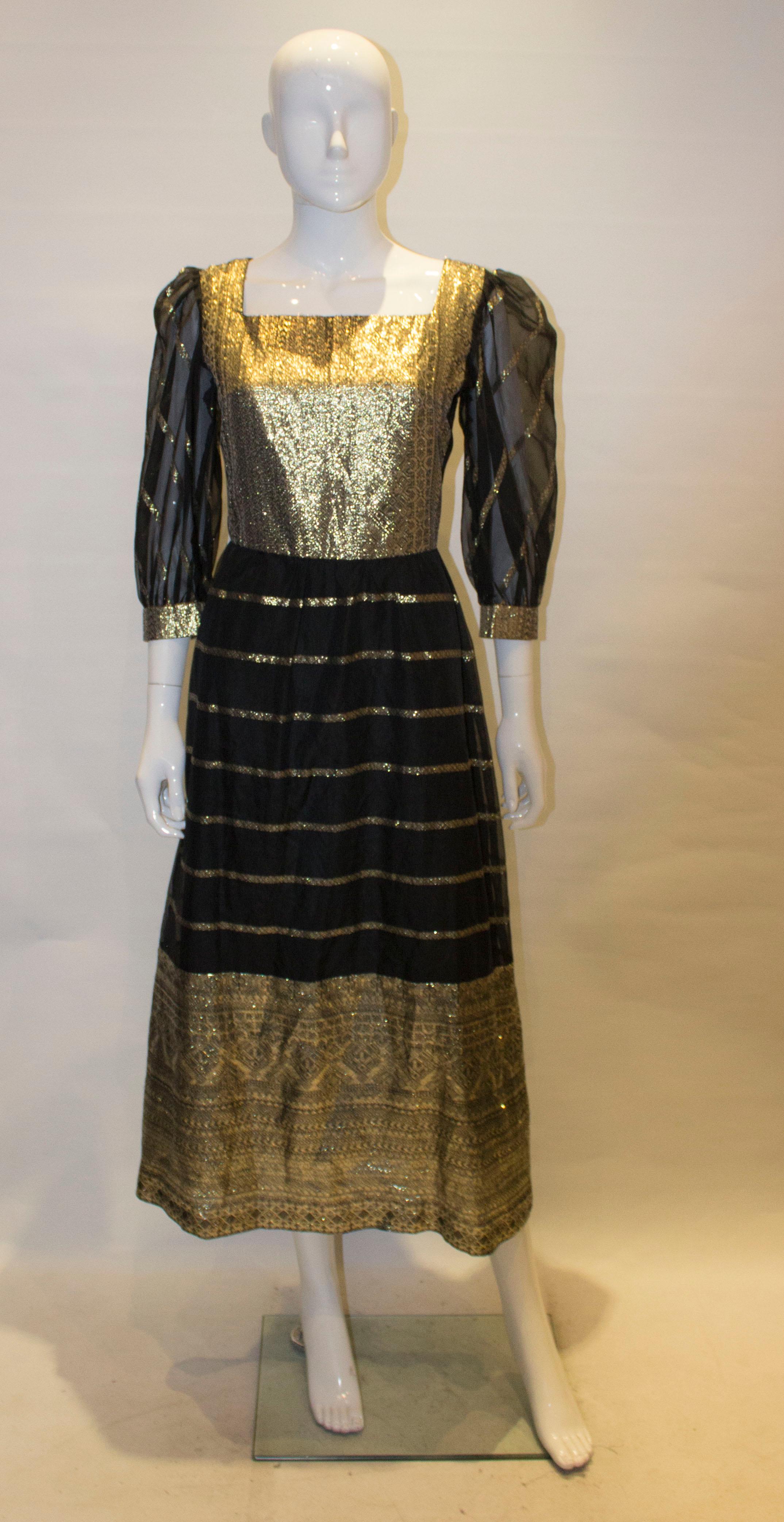 A fun dress from the 1970s. The dress has a gold panel on the front and back , with a square neckline and backline. It has a central back zip, sheer sleeves and gold cuffs, and a gold border at the hem. The dress is lined.