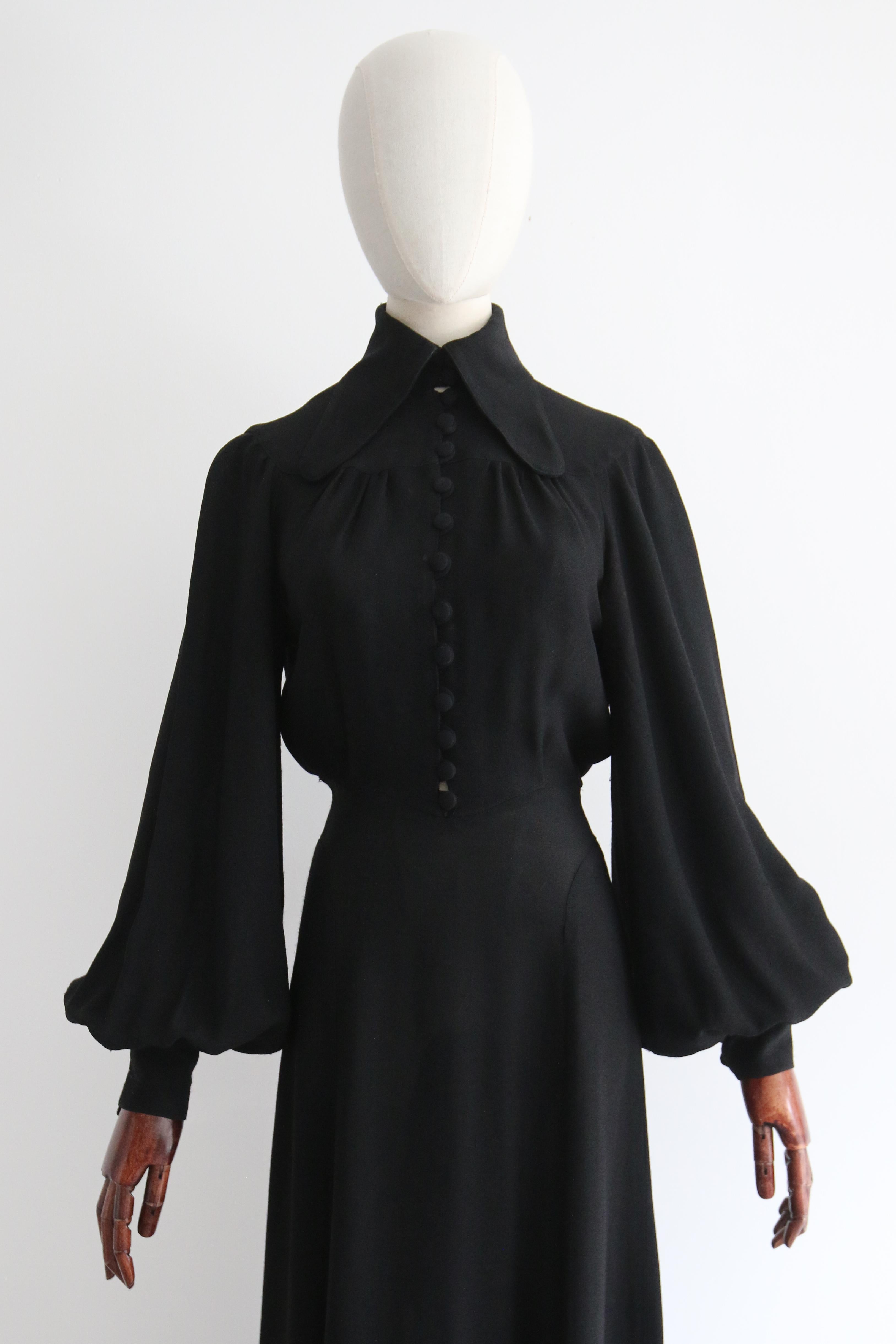 This truly iconic 1970's Ossie Clark moss crepe dress in the darkest shade of black moss crepe, is the perfect piece to add to your collectable and classic vintage wardrobe.  

The rounded neckline of the dress is framed by a wide dog ear collar