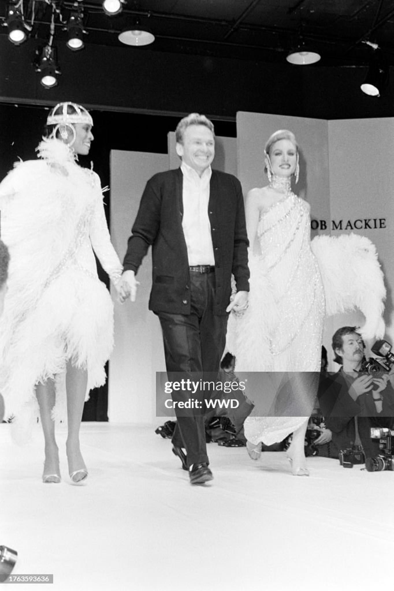 A truly breathtaking and highly coveted Bob Mackie heavily beaded trompe l'oeil ivory silk goddess gown dating back to his documented 1984 fall/winter runway collection. As shown, the beautiful Connie Cook glided down the runway arm in arm with