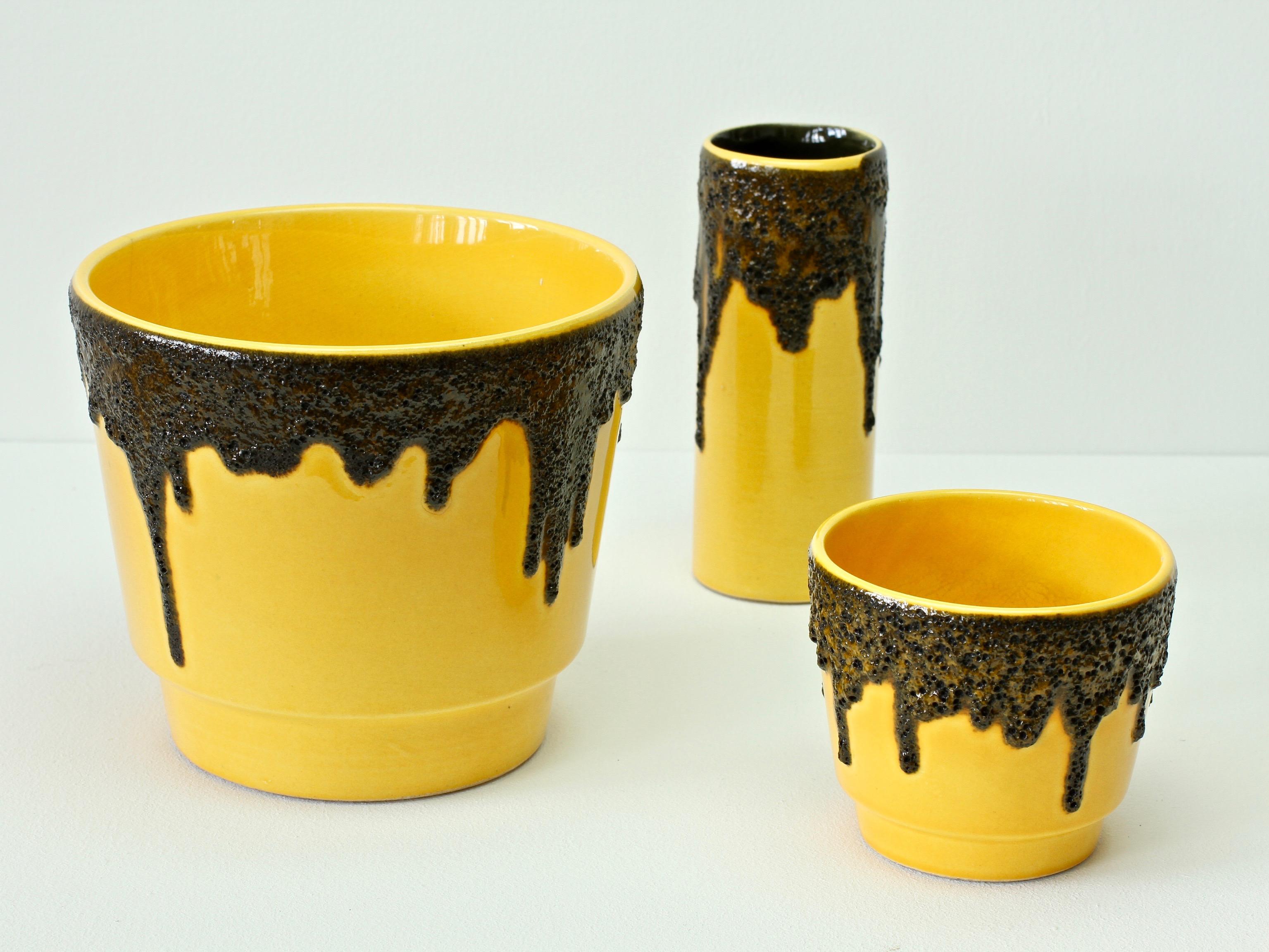 A tall, cylindrical, beautiful and bright vivid yellow vase attributed to Fohr Pottery although similar vases were made by ES Keramik, circa 1970. The bright yellow looks wonderful against the textured black fat lava drip glaze. 

A wonderfully