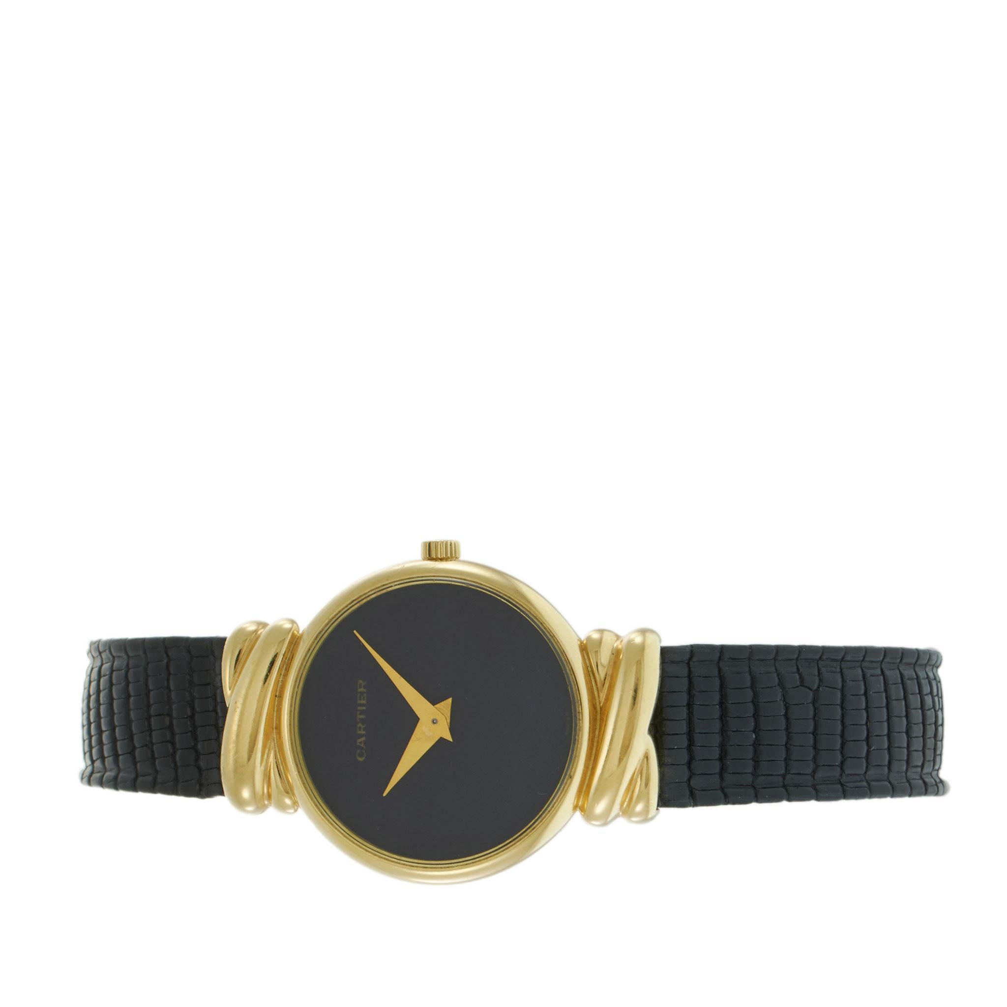 Orologio Cartier vintage degli anni '70 con cassa in oro giallo 18KT da 24,5 mm caratterizzata da eleganti anse in stile fantasia e lunetta liscia e lucida. Il quadrante nero con lancette dorate e design minimalista è animato dal movimento a carica