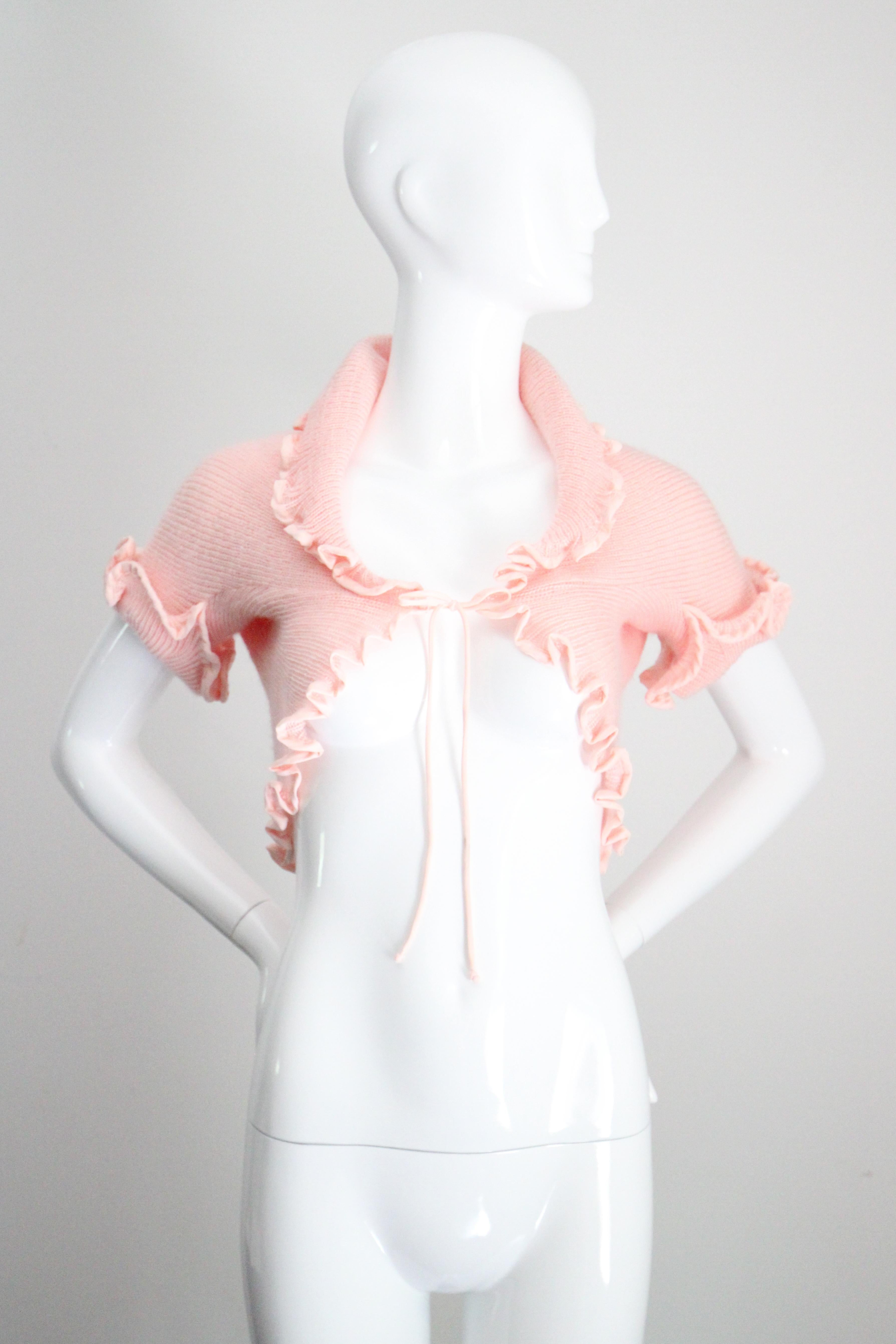Una storia d'amore nella più morbida tonalità del rosa baby, questa giacca da letto in maglia acrilica originale degli anni '70 di Christian Dior è il capo perfetto per tenere lontano il freddo. 

La scollatura arrotondata è incorniciata da un