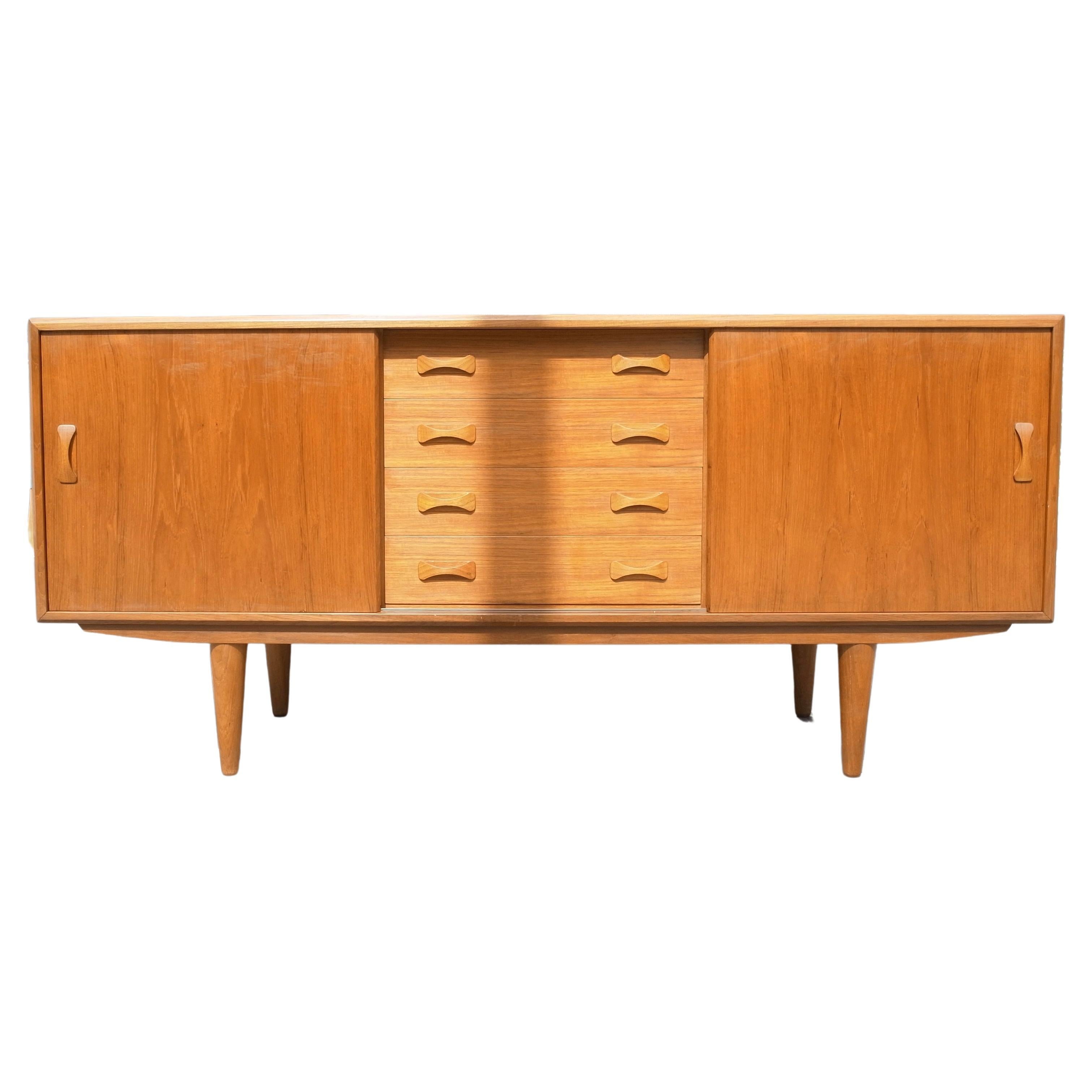 A very stylish and beautifully proportioned vintage Danish 1970s, Teak veneered, sideboard with sliding doors located either side of four drawers, with carved handles and set on elegant solid Teak turned legs, manufactured by Danish company 'Clausen