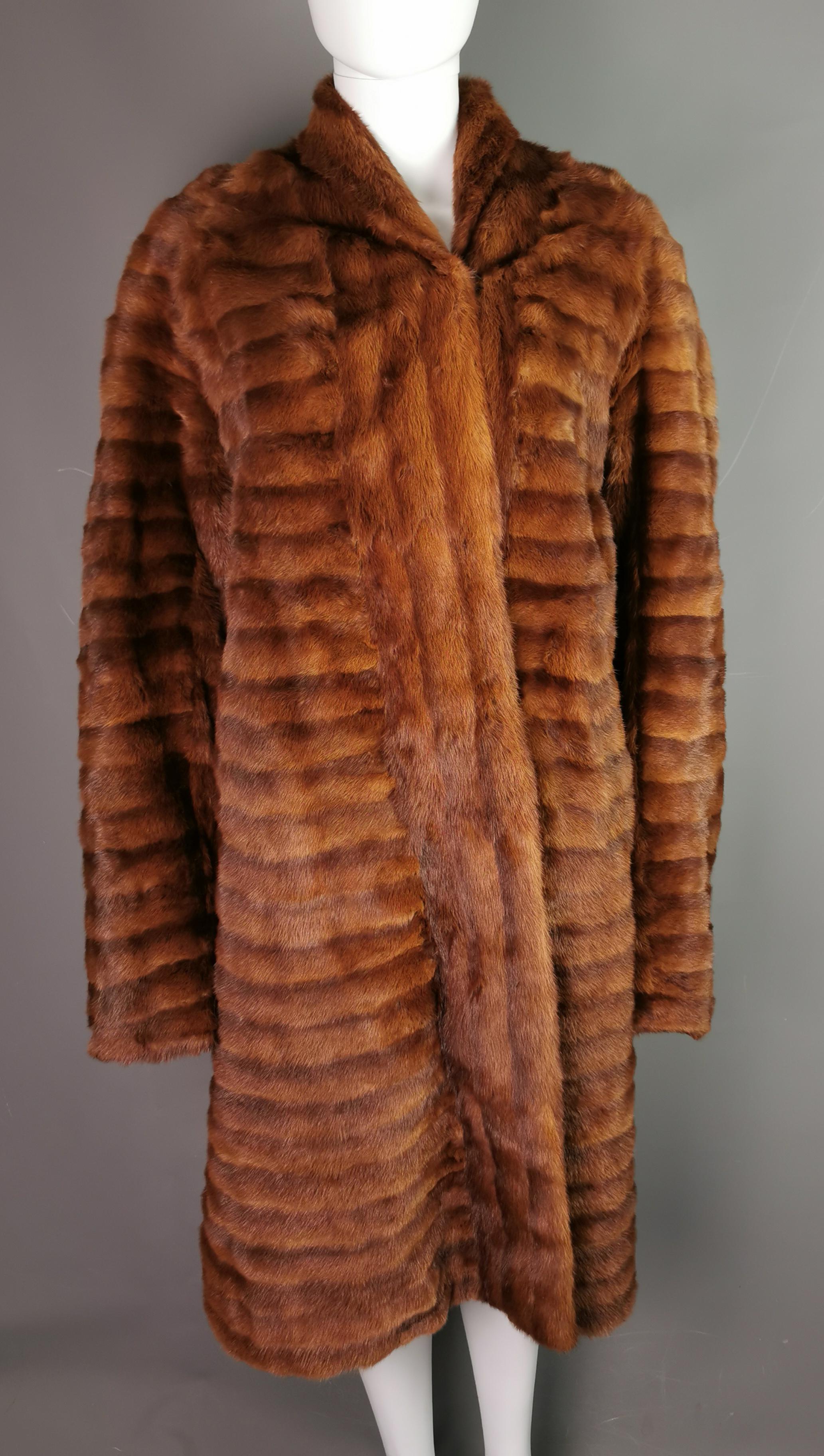 A vintage c1970s coney fur coat.

It is a reddish brown colour, long length with slim sleek pelts.

The coat has a short collar, wrap over style fastening which fastens with fabric covered metal hooks.

The coat has pockets and is lined in a toffee