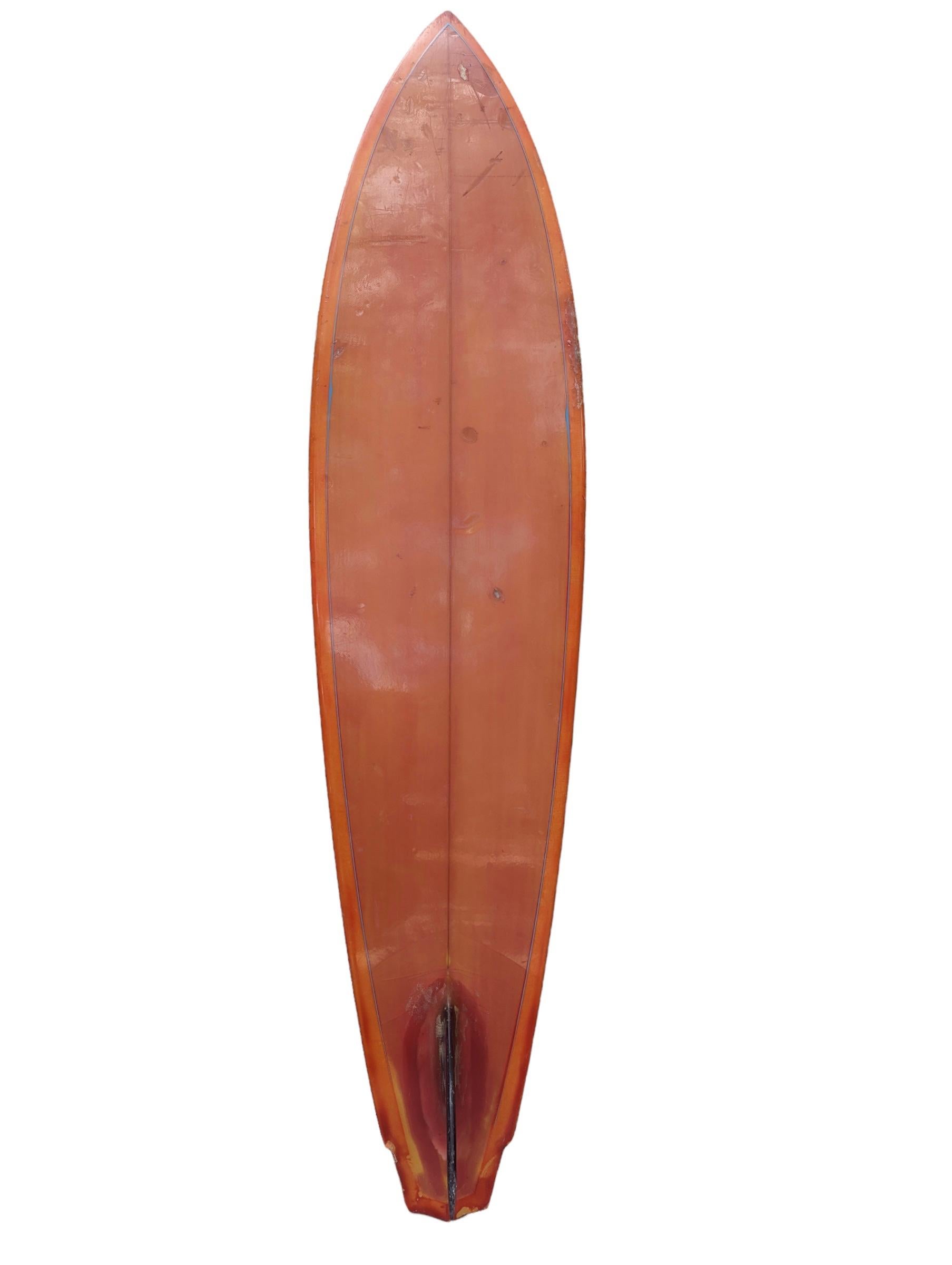 Mid-1970s Dick Brewer surfboard. Features an orange tint with uncommon rocket tail winged shape design. Glassed on single fin with pinstriped outline. A remarkable example of a 70s surfboard made under the coveted label of Dick Brewer Surfboards.