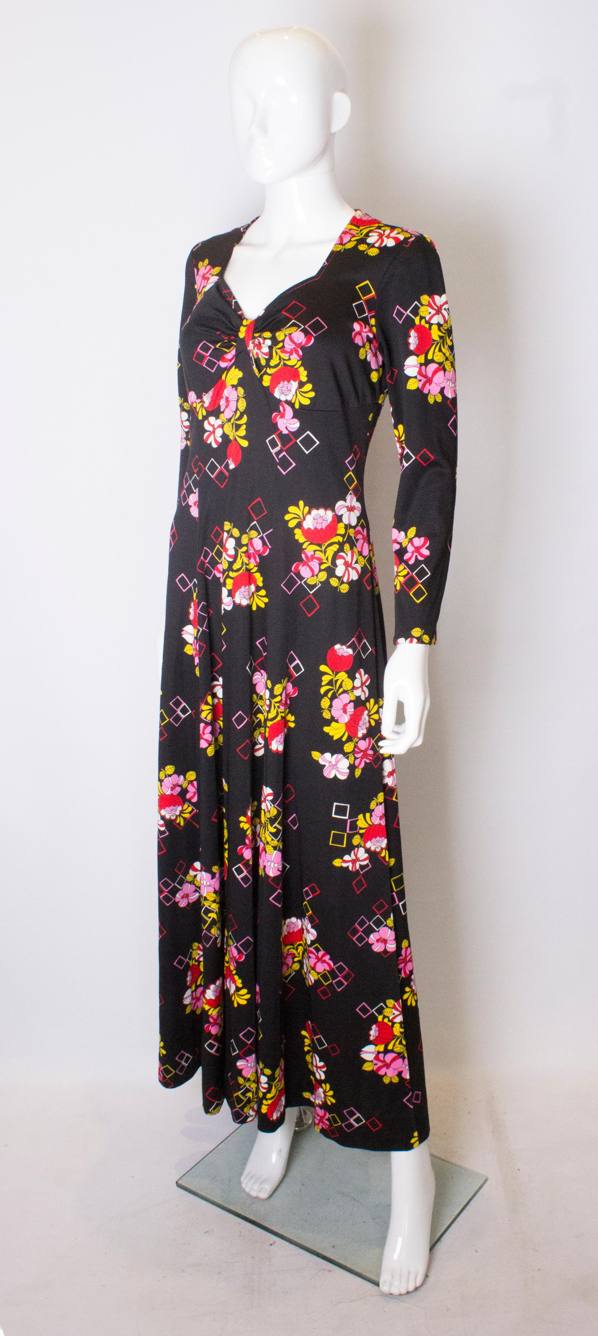 Une jolie robe des années 1970, facile à porter. La robe a un fond noir, avec des motifs floraux en jaune, rose et rouge. Il présente une encolure en forme de cœur et une fermeture éclair centrale au dos.