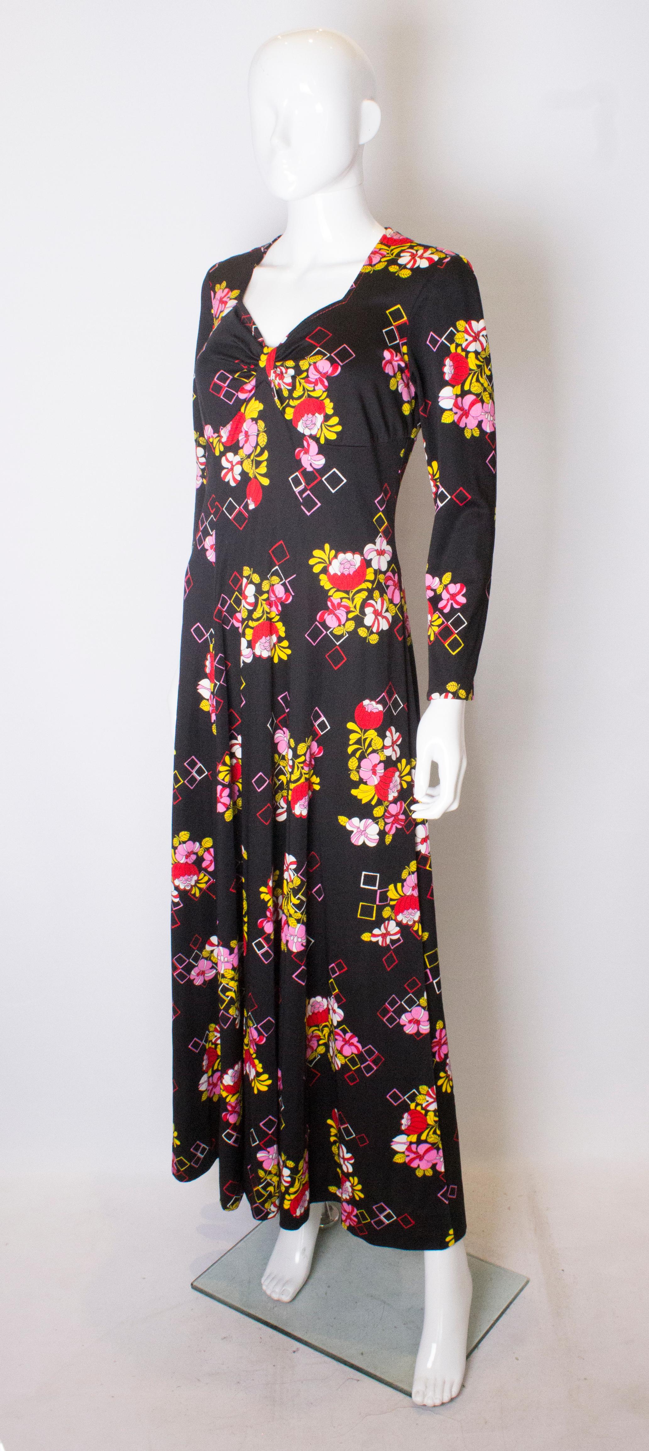 A pretty and easy to wear gown from the 1970s. The dress has a black background, with floral pattern in yellow , pink and red. It has a sweetheart neckline and central back zip.