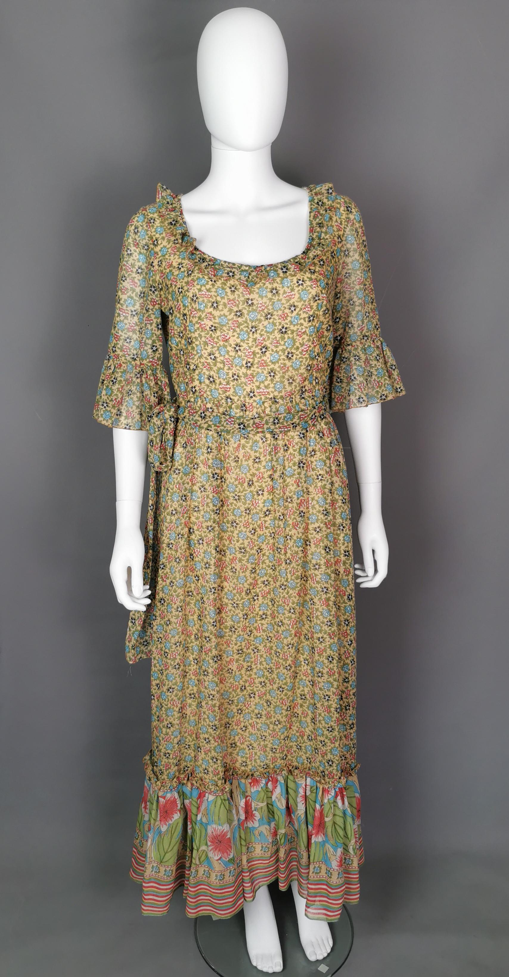 Eine schöne Vintage c1970s floral Maxi-Kleid.

Das Kleid ist aus weicher, leicht durchscheinender, feiner Baumwolle gefertigt, die mit einem floralen Muster bedruckt ist, fast wie ein Zickzackdruck mit einem kontrastierenden tropischen Blumendruck