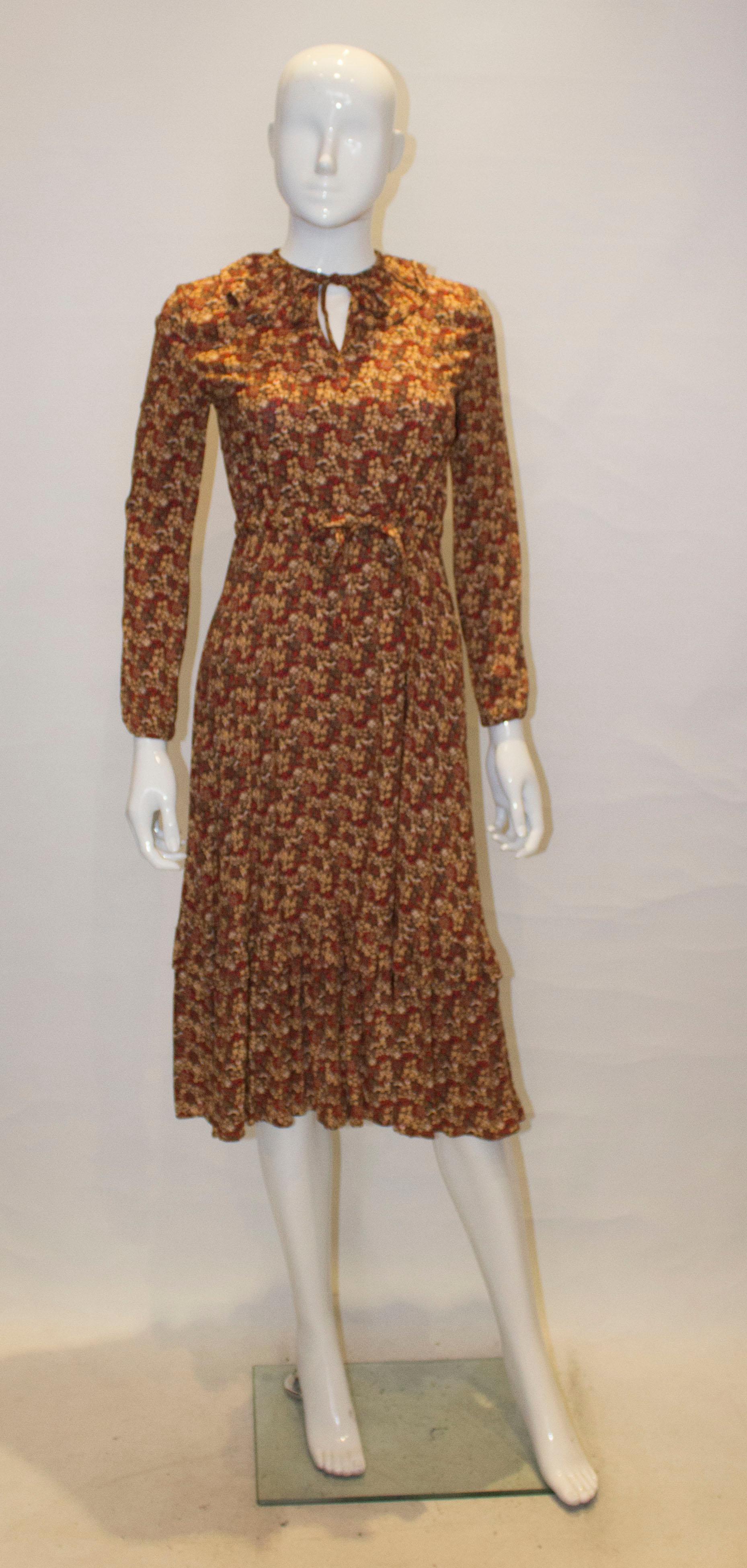 A pretty brown background floral print dress with a frill collar and tie at the neck.  It has a drawstring waist, for multiple sizing,  and frill at the hem.  The waist will fit up to 32''. Bust 34'' , length 46''.