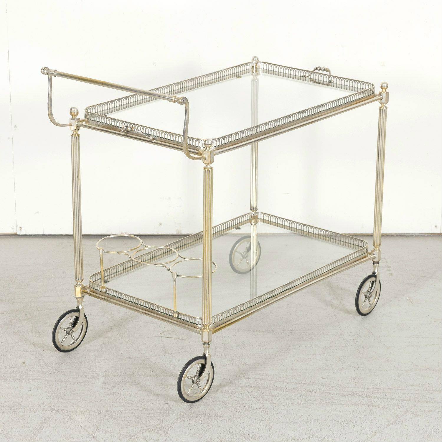 A handsome vintage French silver plated two-tier rolling bar cart or serving trolley, having a detachable pierced gallery glass service tray with handles on upper tier and a pierced gallery glass shelf with bottle rack for three bottles on lower