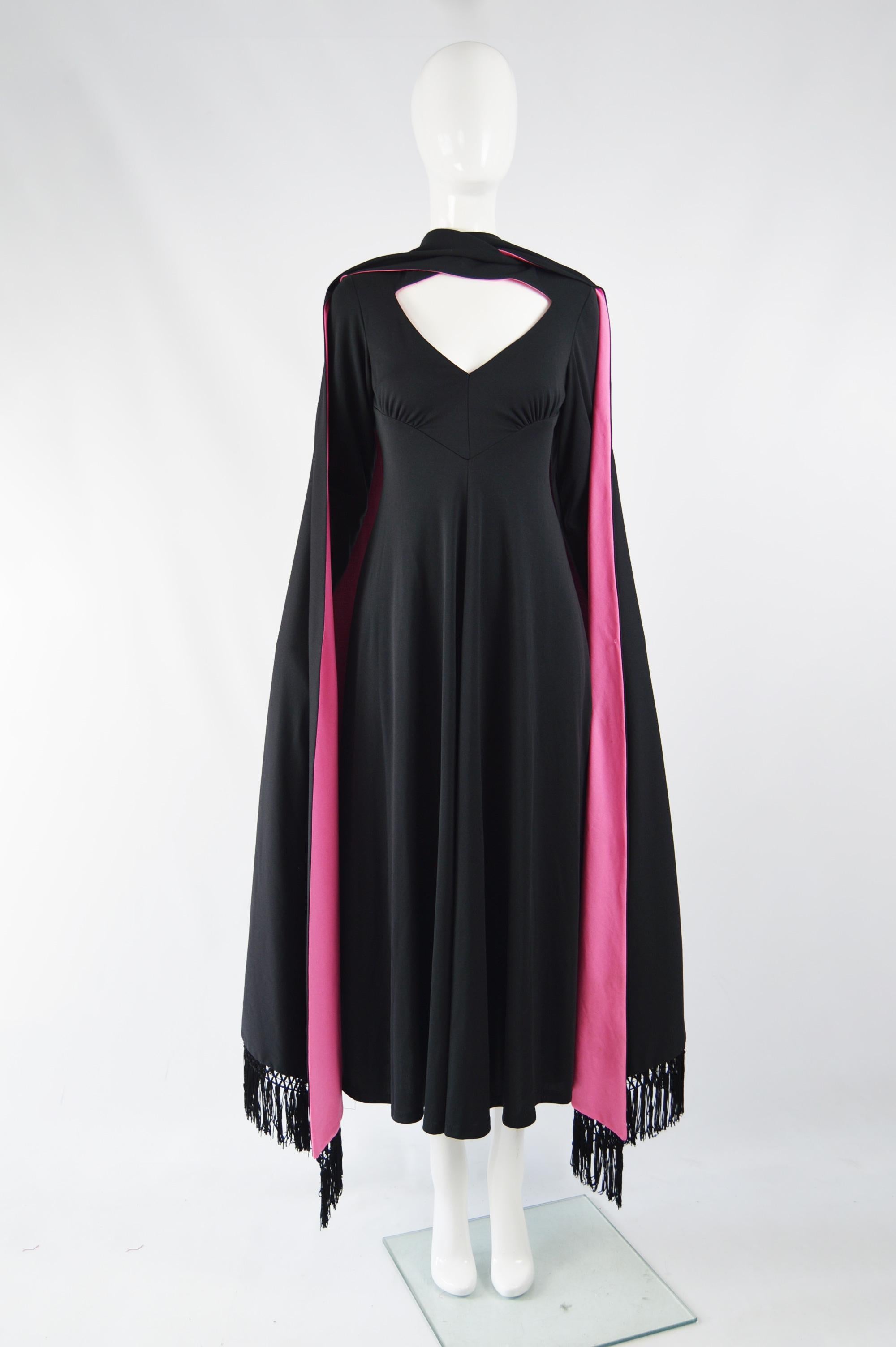 A fabulous vintage womens maxi evening gown from the 70s by quality British label, Ronald Joyce. In a black and pink synthetic jersey with long, fringed cape / train details at the back of either shoulder. Perfect for a red carpet or formal party,