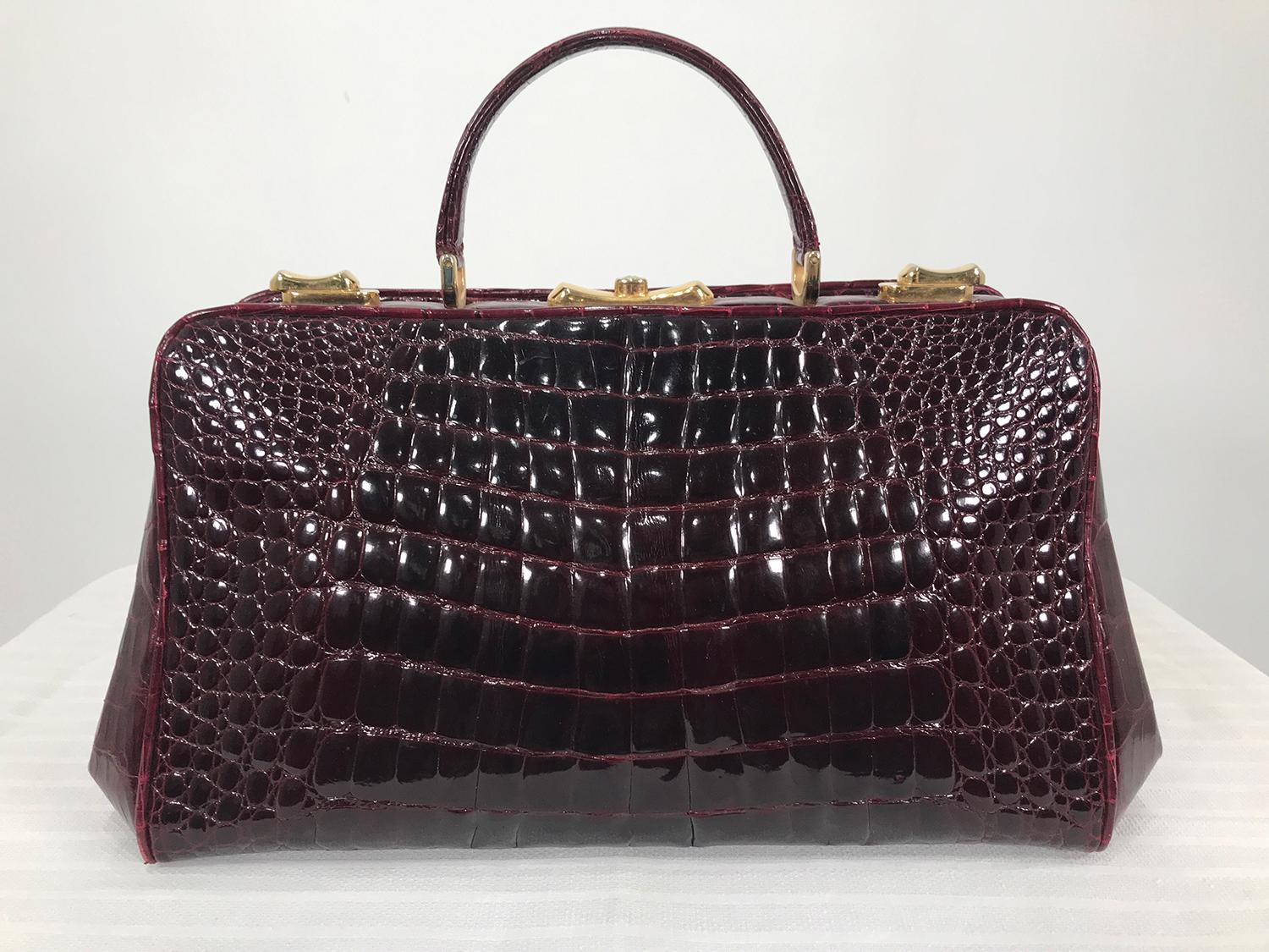 Vintage 1970s  glazed burgundy alligator satchel with gold hardware. This beautiful frame handbag has a single handle, the bag has gold hardware consisting, top side locks, center push lock with key, handle attachments and 6 feet at the bottom. The