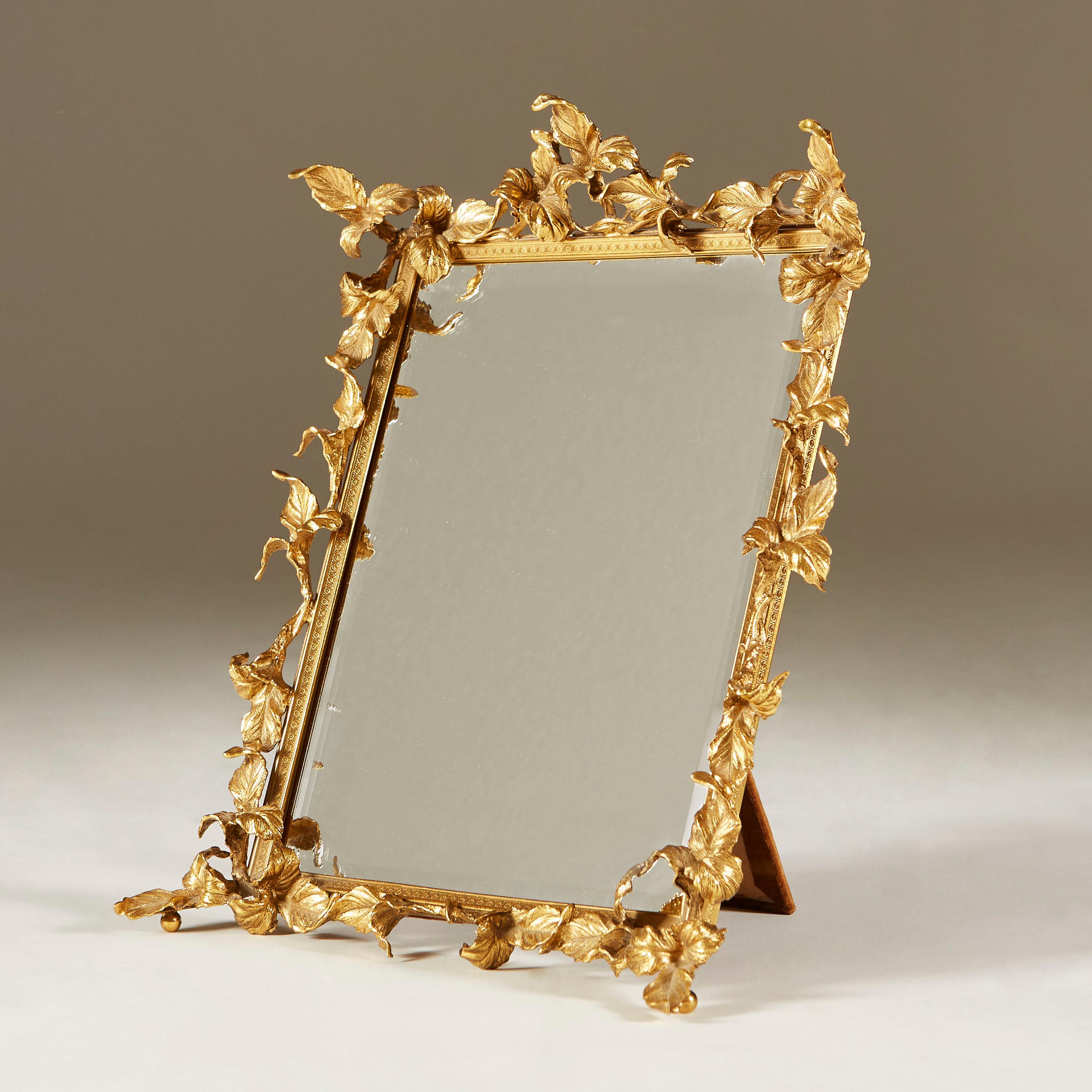 Decorative gold table mirror surround with cross-cross patterned frame and intricate leaf detailing. Sits on ball feet. Velvet back and back strut. Bevelled edge mirror. Perfect for the dressing-table or anywhere other that needs a touch of