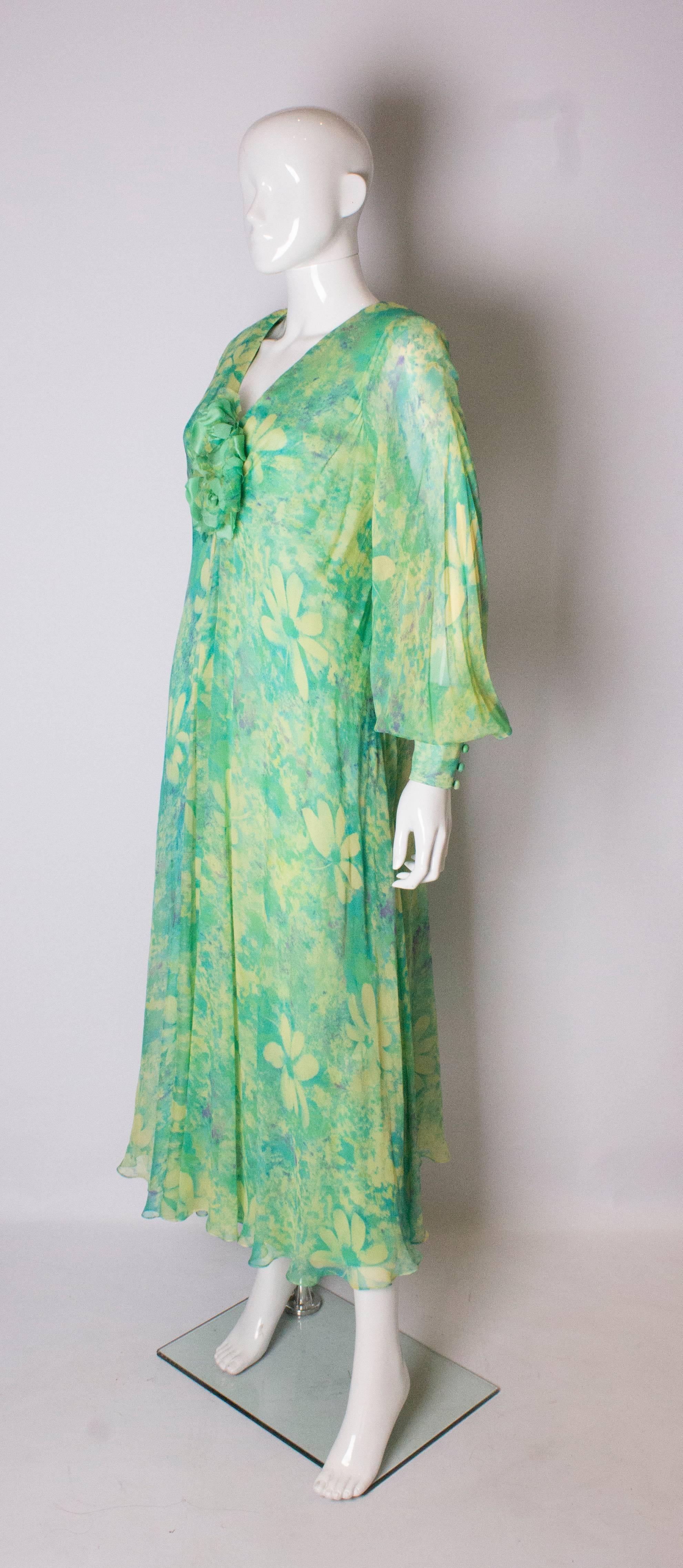 A pretty and easy to wear vintage dress by Alison Rodger. The dress has a silk chiffon over dress in a yellow, green and blue floral print It has a silk underdress t and is lined in silk. It as a central back zip with a pleat on either side, and