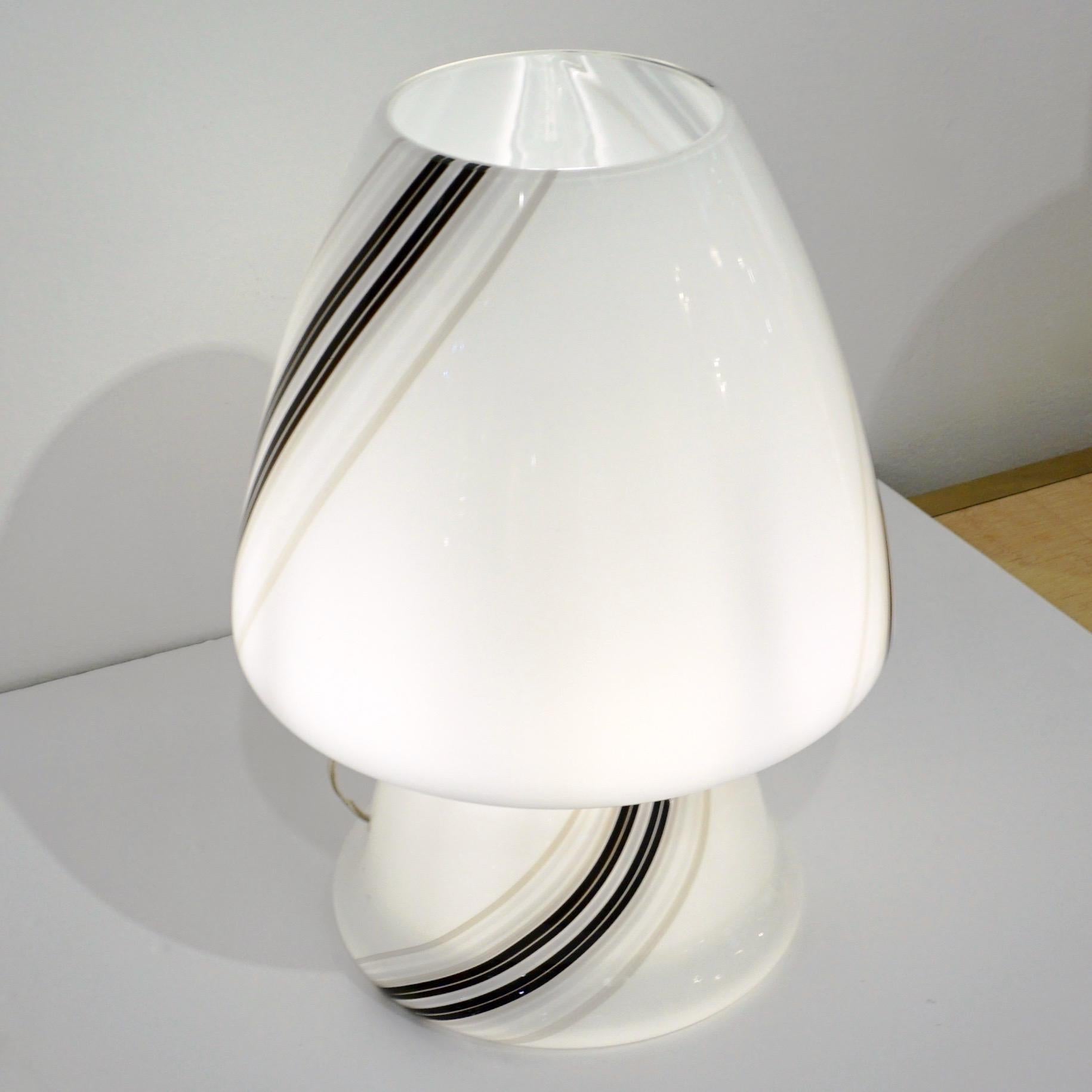 A delightful mid-20th century modern Italian design table lamp, attributed to Vistosi, of organic conical mushroom shape, skillfully blown as a whole single piece in white Murano glass artistically decorated with elegant swirling black and grey