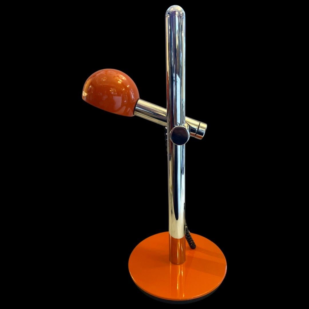 The vintage 1970's vibrant orange desk lamp is a captivating blend of retro charm and contemporary flair. Its striking hue immediately commands attention, while the chrome stem and arm add a touch of  contemporary elegance, creating a harmonious