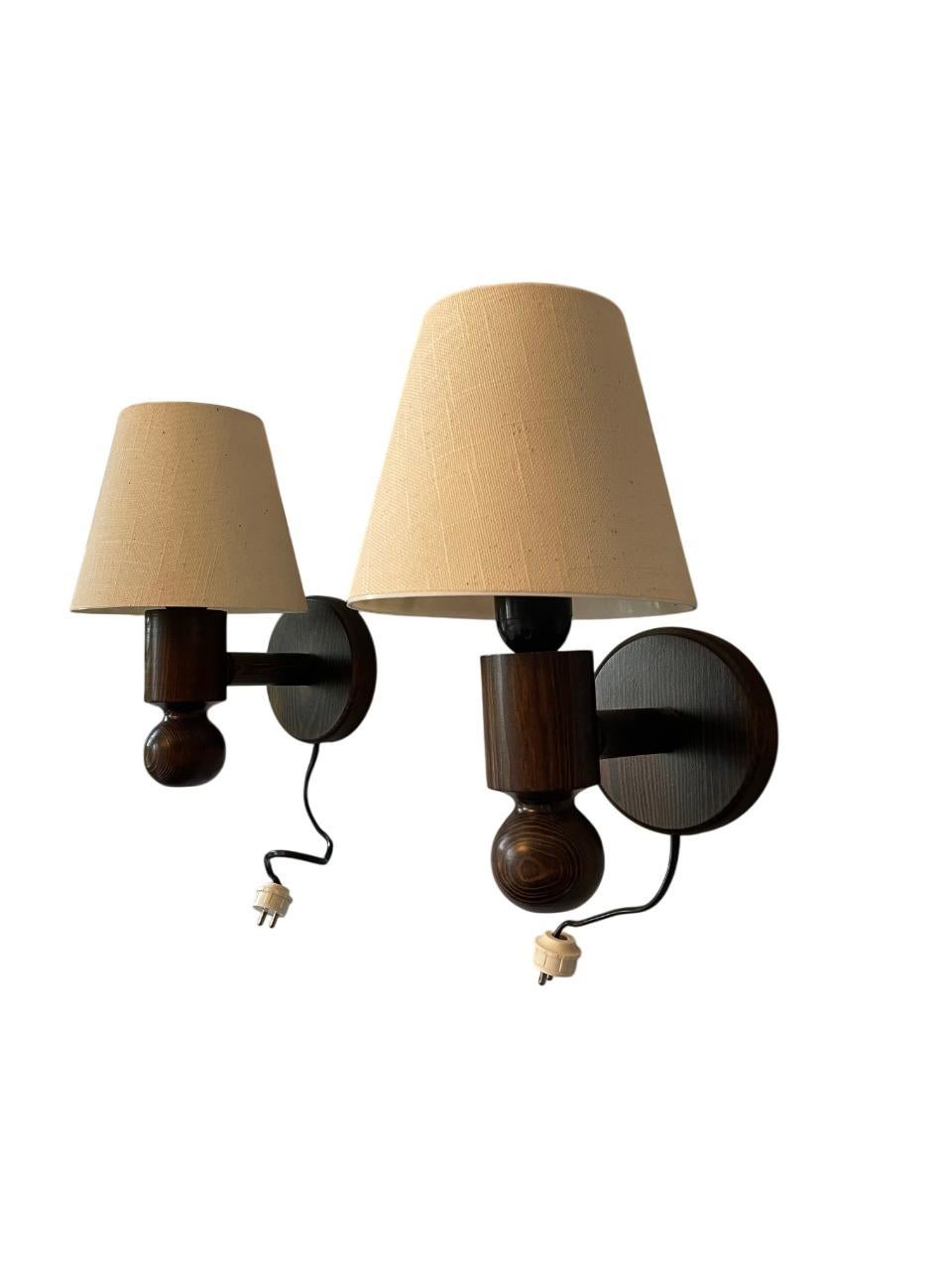 Un magnifique ensemble de cinq lampes murales originales de Markslöjd, fabriquées en Suède dans les années 1970. Ces luminaires scandinaves classiques sont dotés de bases en bois de pin richement teinté et d'abat-jours en tissu beige texturé,