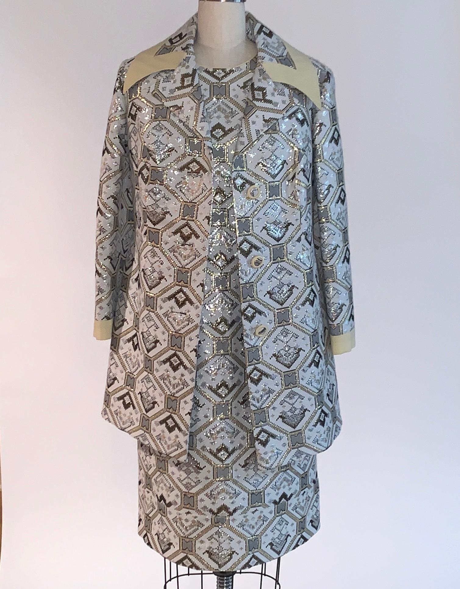 Stunning vintage 1970s short sleeve shift dress and coat set set in white, gold, and silver metallic brocade. Dress has golden yellow piped trim at neck and closes with back zip and hook and loop. Lined in silky material. 

Coat features a wide