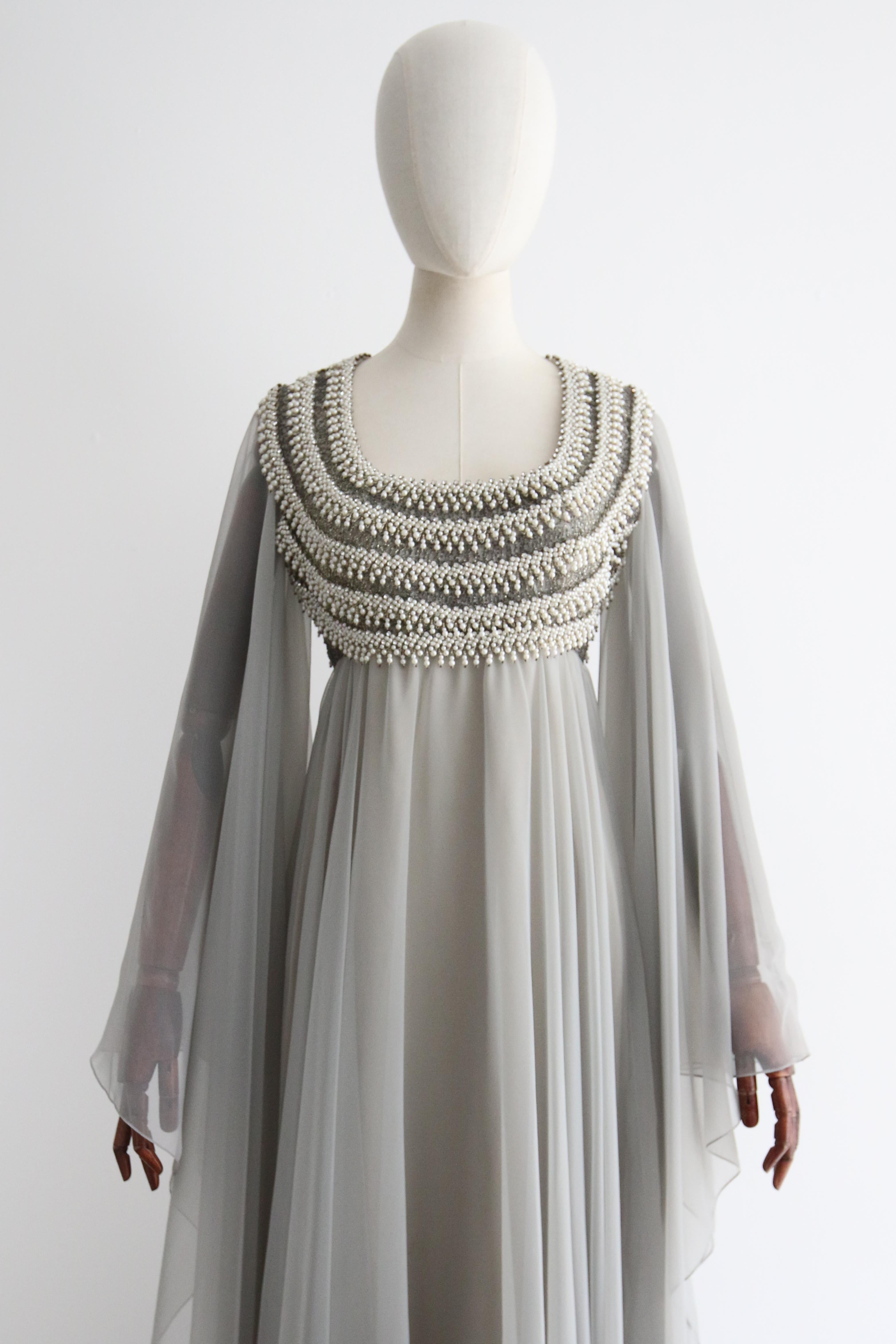Made in the softest shade of dove grey chiffon and embellished with silver glass beads, silver rhinestones, and pearls, this mesmerising 1970's dress, in a pleated and draped design, is just the statement piece you were looking for. 

The rounded