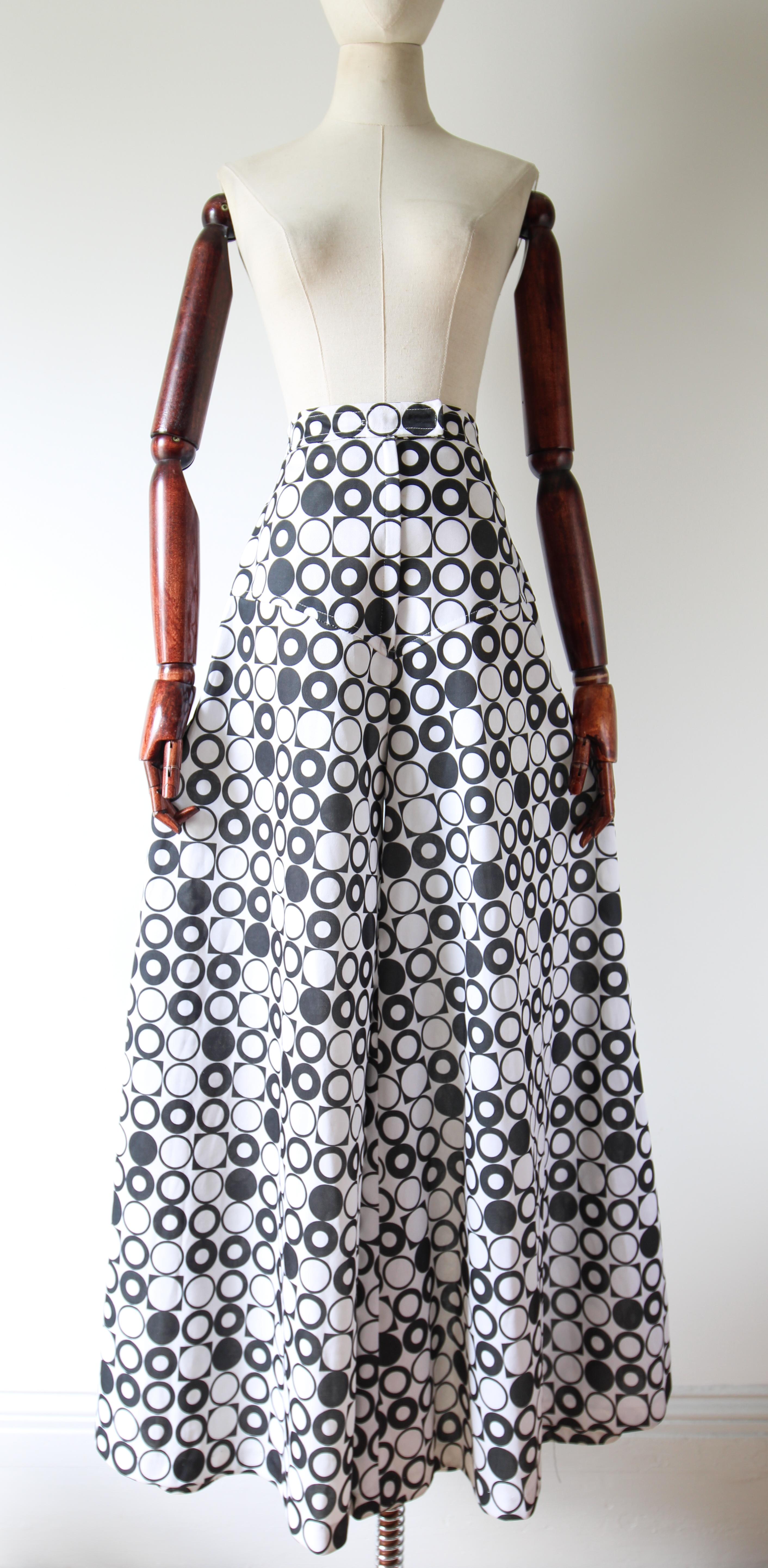 Diese auffällige Hose aus den 1970er Jahren, die in einer monochromen Farbpalette aus schwarzen und weißen Kreisen und Quadraten gehalten ist, ist das perfekte Accessoire für Ihre Garderobe. 

Die hoch geschnittene Hose hat einen einfachen Bund und
