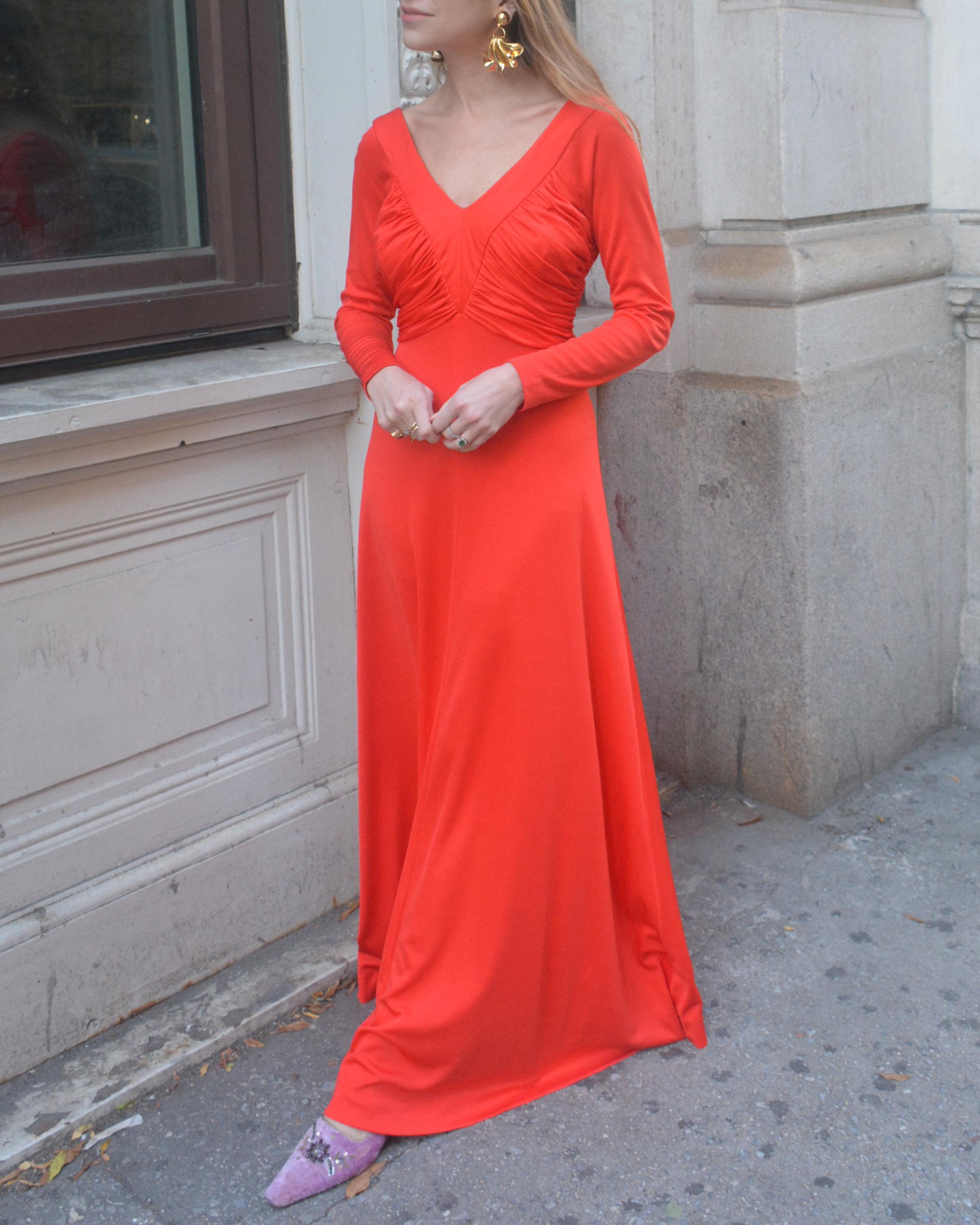 A classic 1970s maxidress, in a fiery orange color: this dress has the silhouette of a gown with the casual elegance of jersey fabric. The color is kind of magical, and difficult to capture in an image: it is not neon but is very saturated and deep.