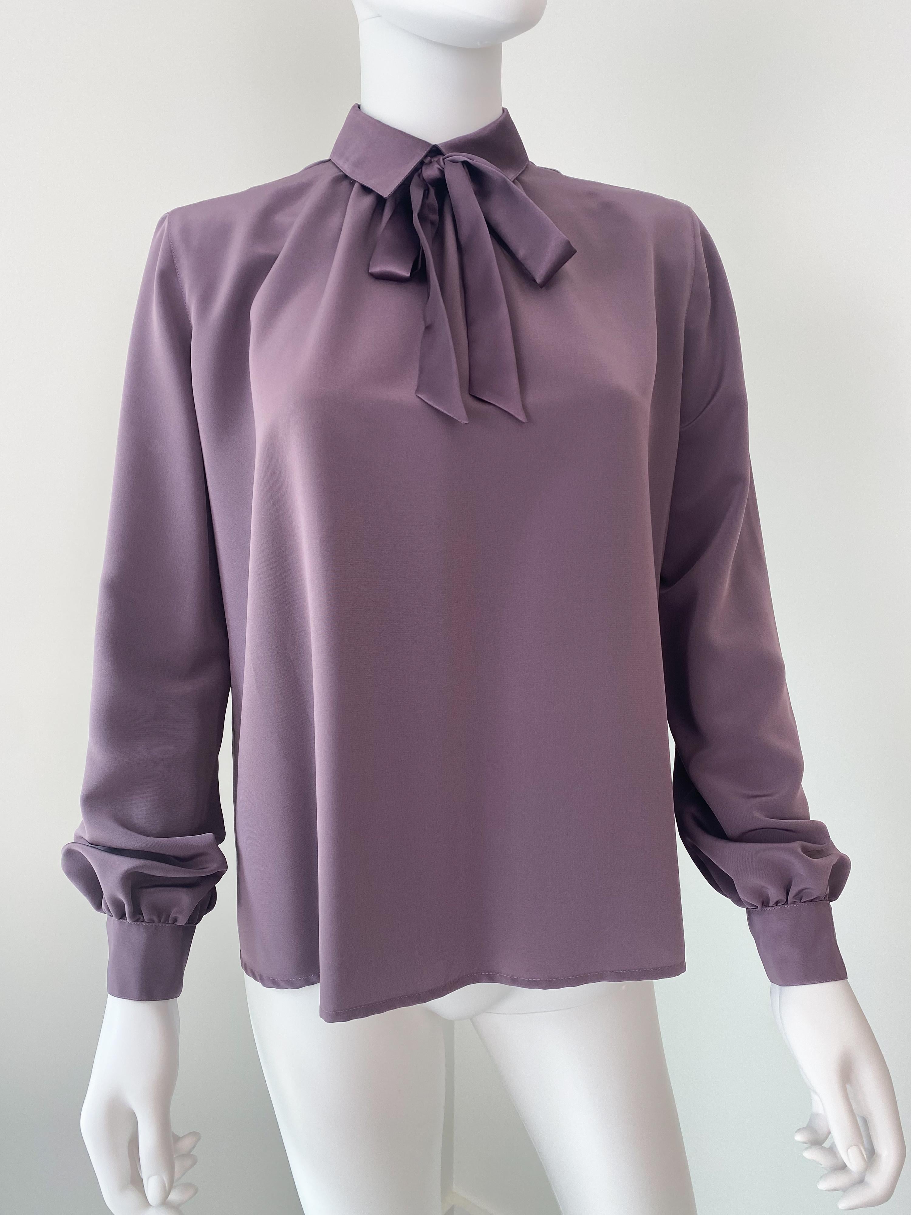 Fabuleuse blouse vintage des années 1970 en polyester soyeux. Le tissu de couleur prune violette contraste avec le col et le nœud en satin de même couleur. Les boutons de fermeture se trouvent à l'arrière. Les poignets boutonnés sont légèrement