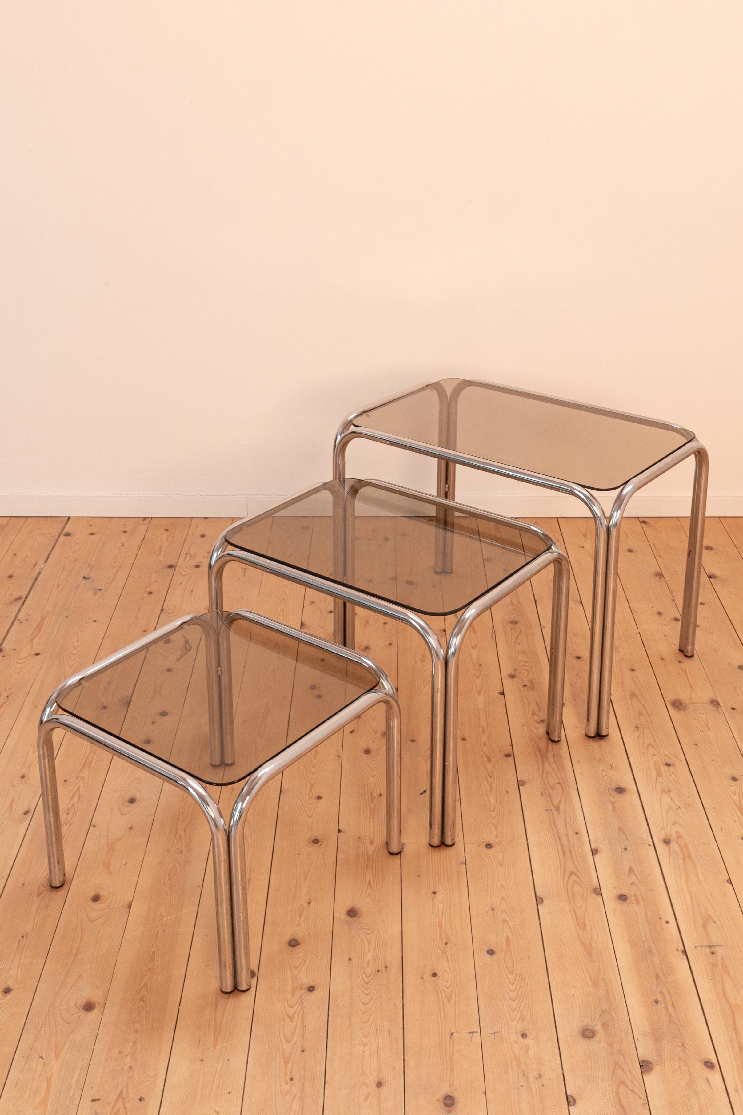 1970s set of 3 smoked glass nesting tables with tubular metal frame. Design after Milo Baughman. The dimensions mentioned are for the largest table. 
The price is for the set of 3 tables