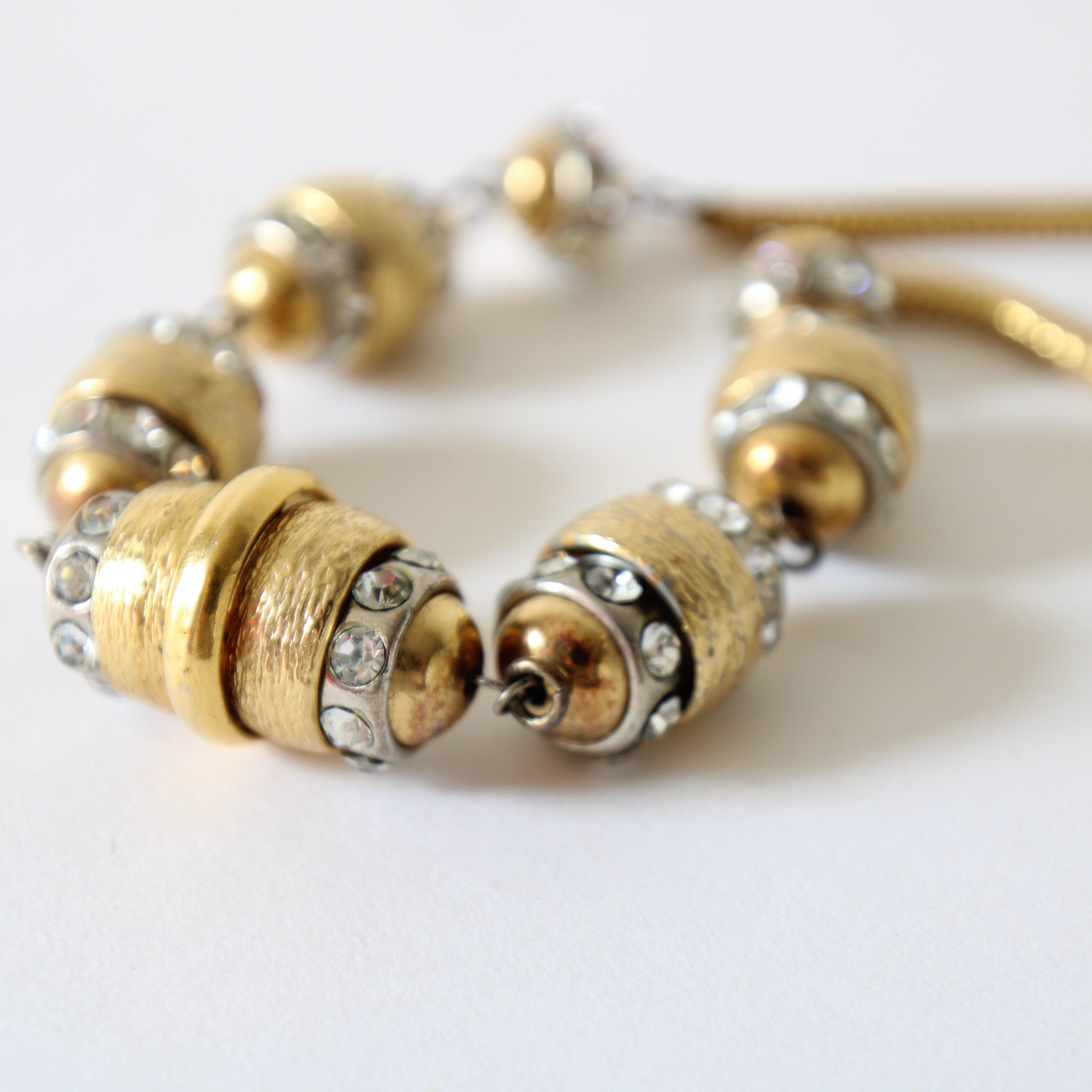 This sparkling 1970's statement necklace, on a gold toned snake chain, linked to 7 gold and silver oval and circular beads, accented by silver set rhinestones and textured gold spacers, is the perfect finishing touch to your outfit. 

 Length: 16