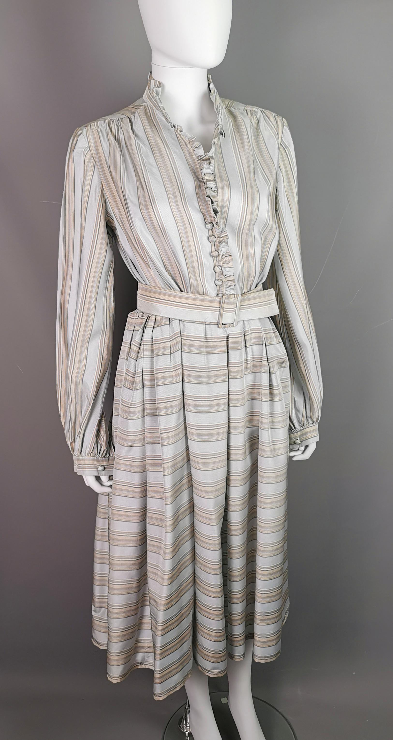A gorgeous vintage c1970s pure silk shirtwaist dress.

It is a mid length dress with long bishop style sleeves, a v neck ruffle neckline and a full skirt.

The dress has a matching belt making the pulled in waist look seamless.

It has a striped
