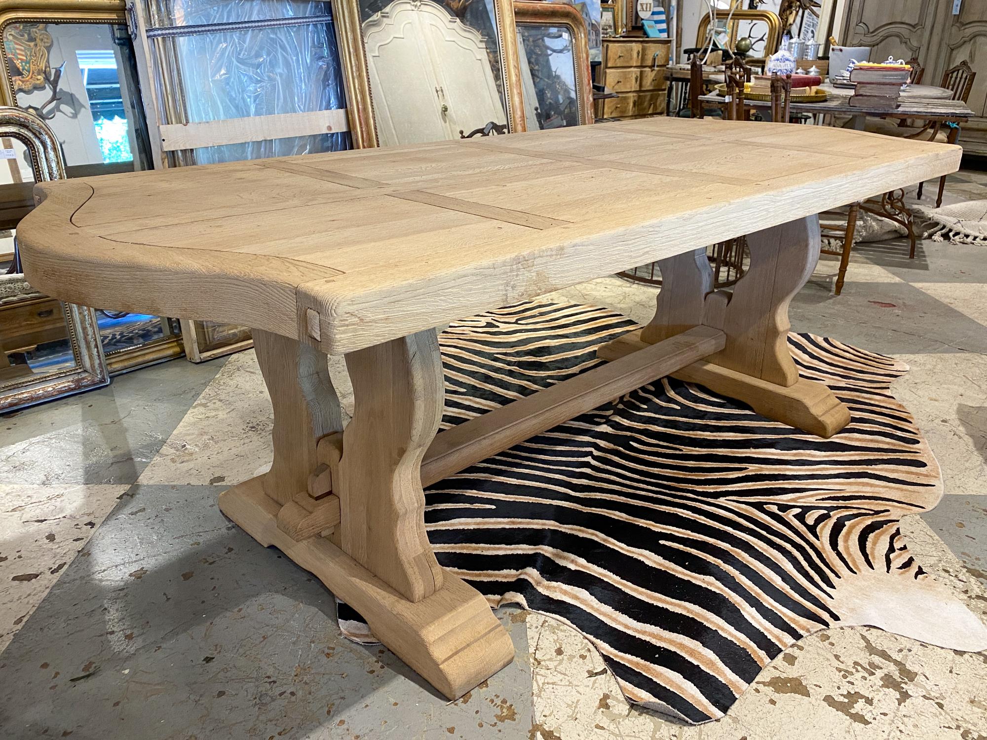 This is a vintage French oak dining table with a trestle style base and a curved edge tabletop. The top of this table also features a paned design pattern. The base and top can be separated for transport. The legs are joined with a solid rail which