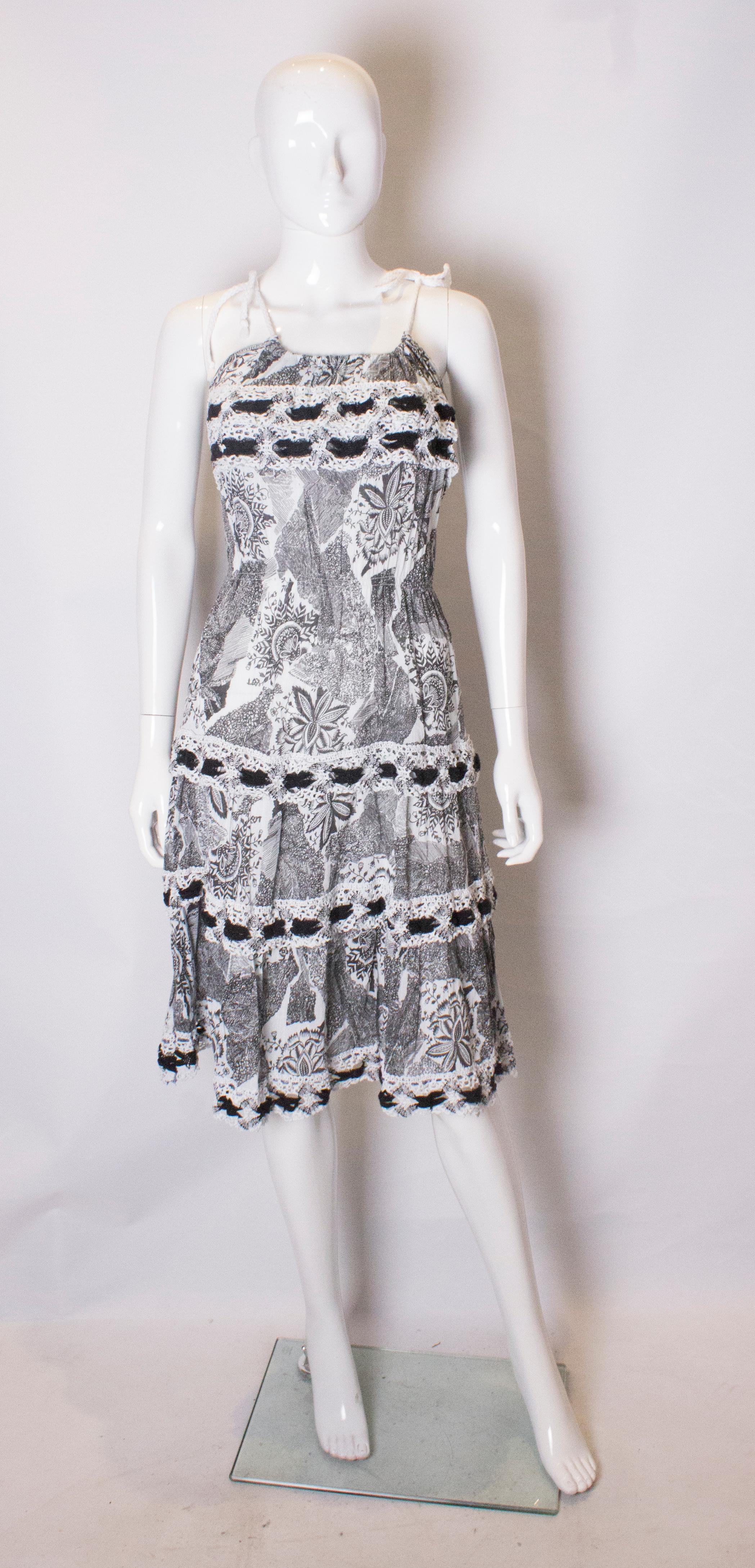 A fun summer sun dress. The dress is in an attractive abstract black and white print. It has white  cord shoulder ties, with an elastic waist ( best 24 -27'') and crochet detail trim.