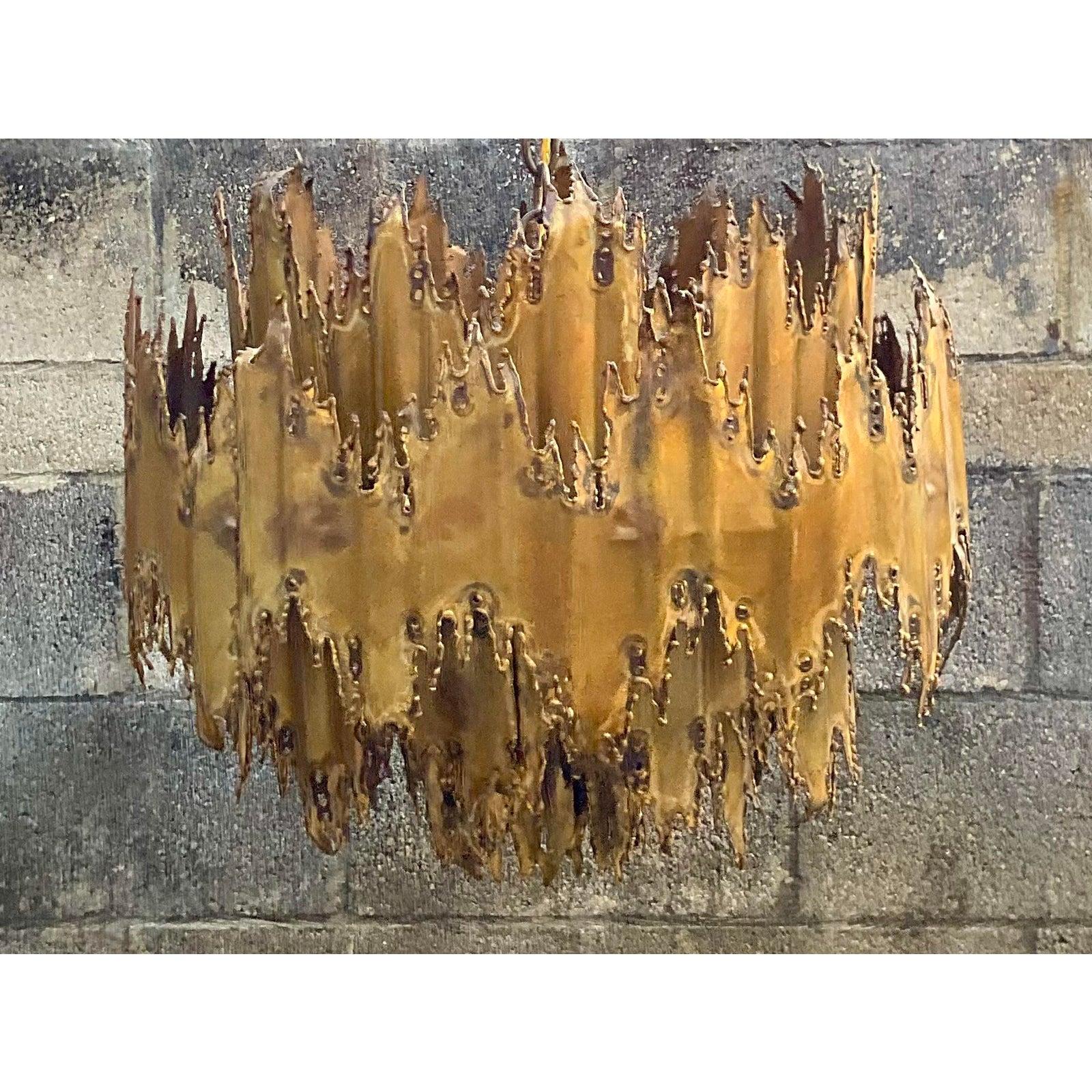 A fantastic authentic Tom Greed chandelier. Striking torch cut edges make this chandelier a real work of art. Five layers of brass with brilliant patina. Brutalist flush mount cap. Unmarked. Acquired from a Palm Beach estate.