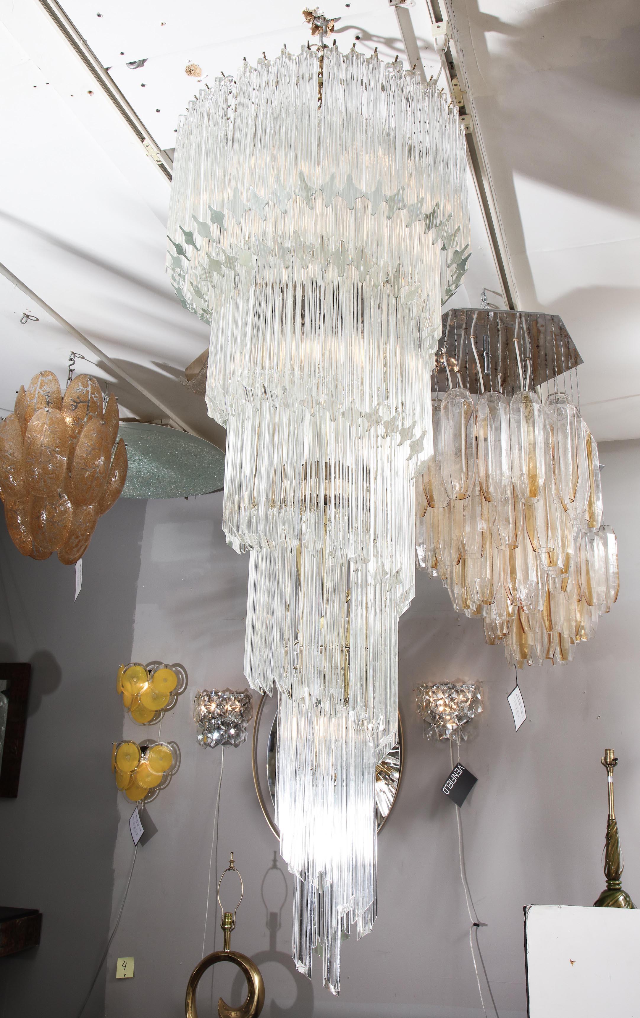 Glamorous vintage quadriedri Venini glass spiral chandelier from 1970s. It is a beautiful cascading 6 tiered chandelier with clear quadriedri glass pieces that creates statuesque silhouette and spiral motion. The frame is in light brass finish and