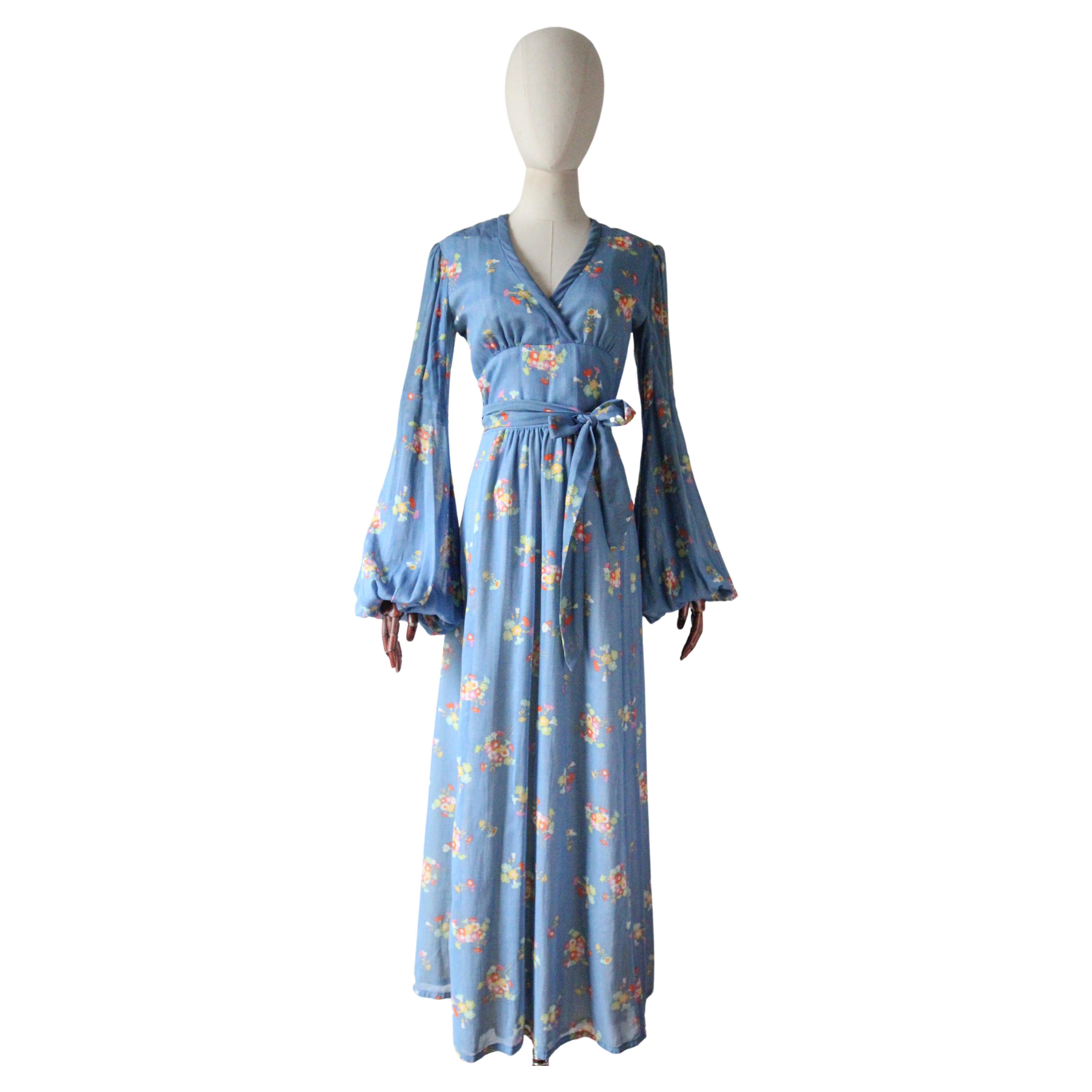 Questo spettacolare abito in voile di cotone azzurro anni '70, caratterizzato da un motivo a grappoli di fiori nelle vibranti tonalità del giallo, del rosa, dell'arancio, del bianco e del verde, costruito con un design incredibile e ipnotico, è un