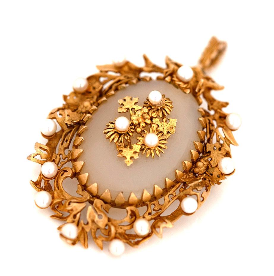 Vintage 1970s gold pendant brooch crafted from a polished chalcedony cabochon set in a stunning bright yellow 9ct gold mount adorned with pearls. A central solid gold element with three floral parts, the intricate openwork frame of the gold mount