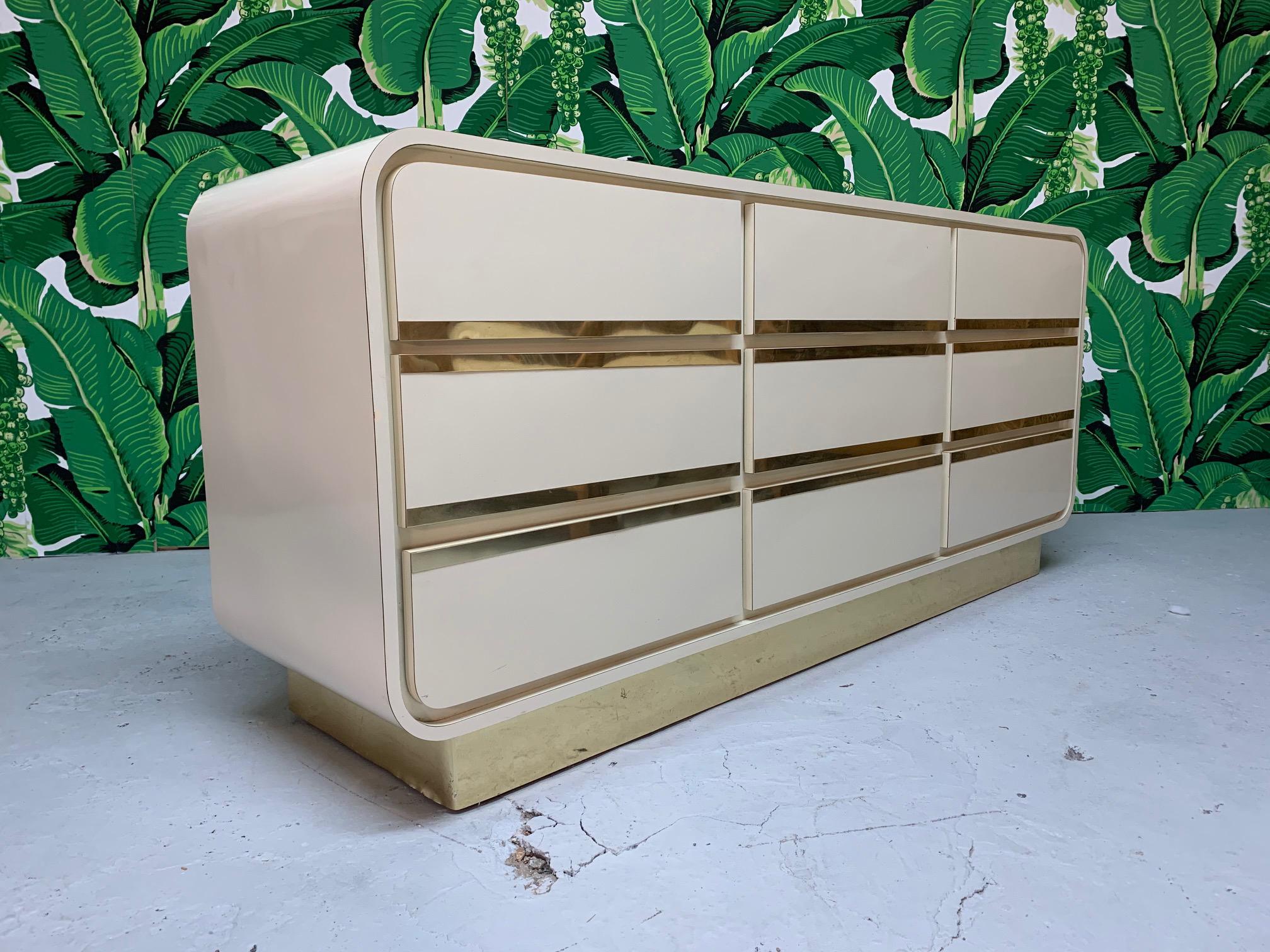 1980s art deco style dresser features waterfall shape and brass detailing on drawer fronts and a brass plinth (brass shim veneer). Very good vintage condition with minor imperfections consistent with age.